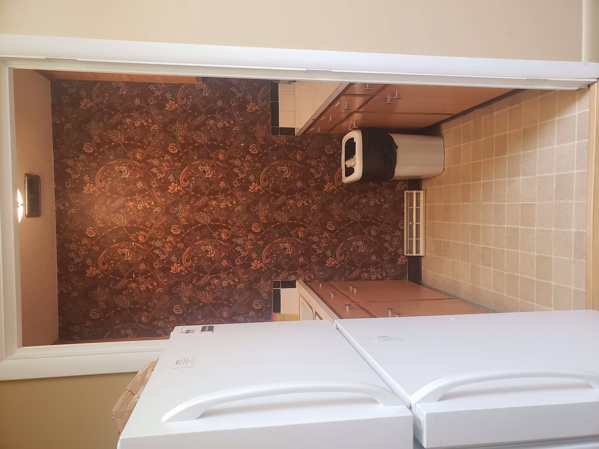 A compact utility space with washers, cabinets, and patterned wallpaper in a senior living facility.