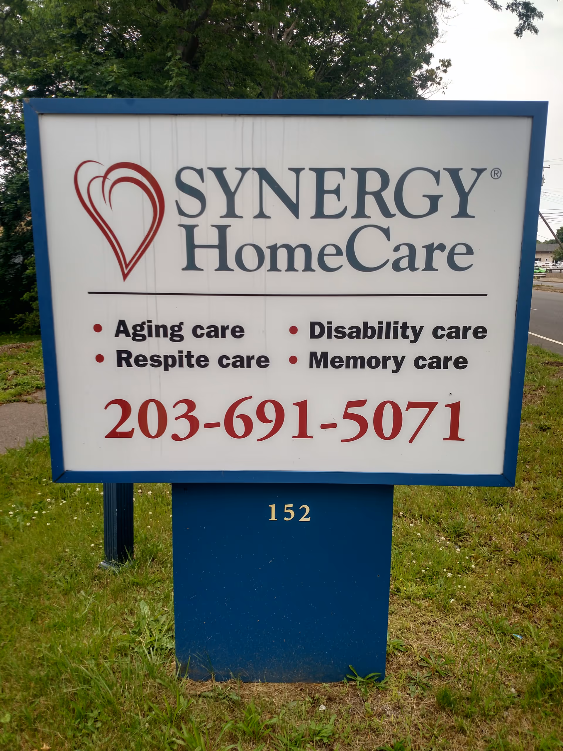 Outdoor view of a SYNERGY HomeCare sign listing services and a phone number.