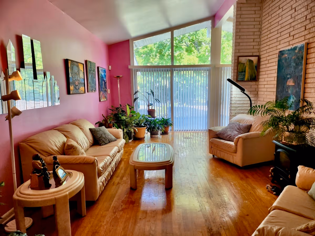 Bright pink-walled living room with beige sofas, plants, and large windows.