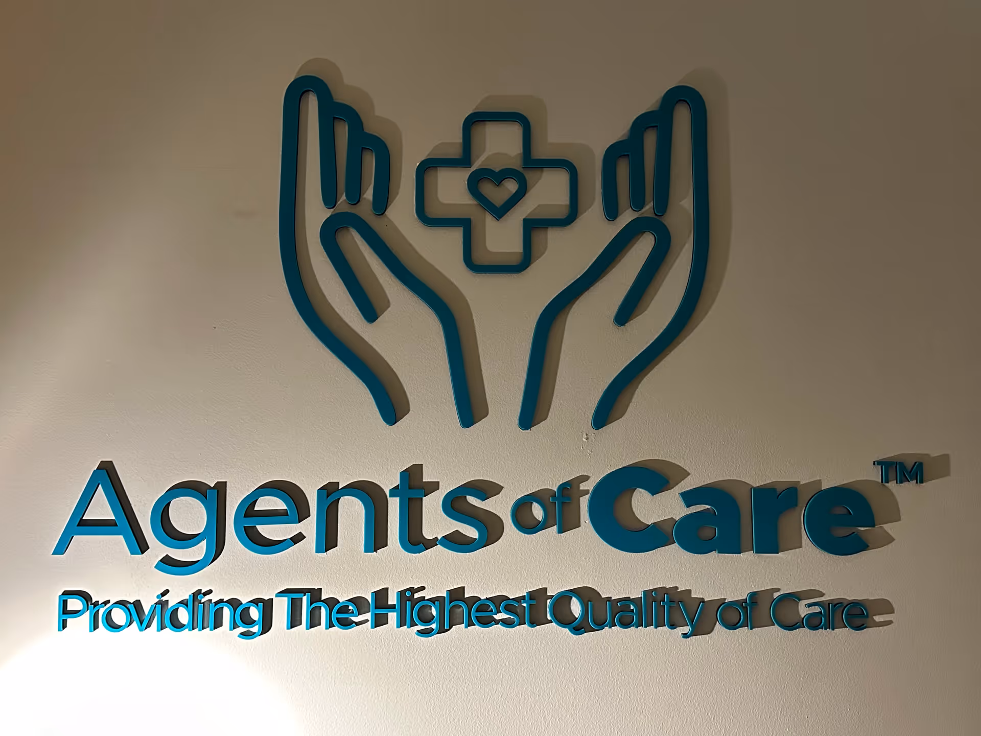 Interior wall sign for Agents of Care featuring teal hands logo and slogan.