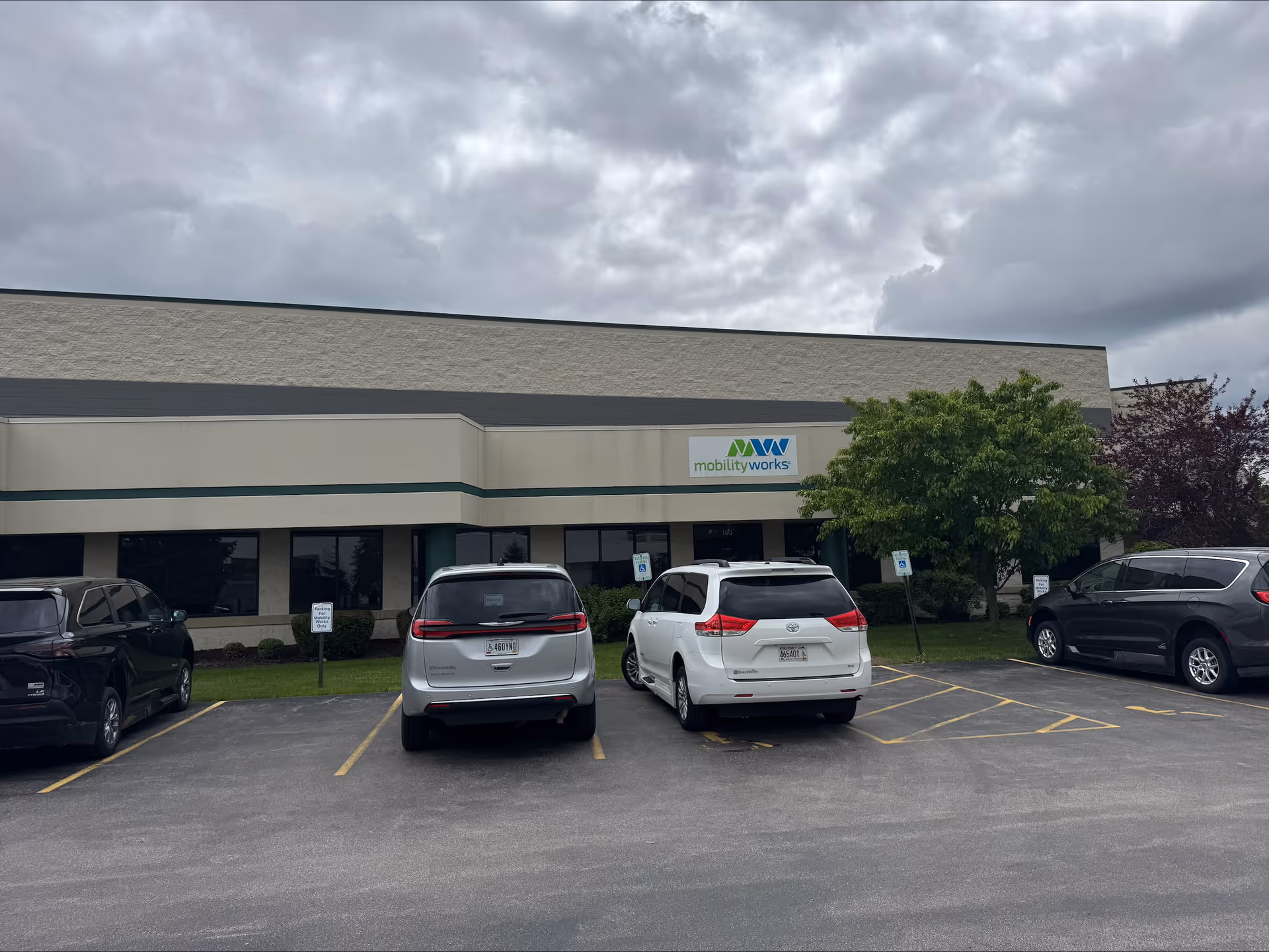 Front view of MobilityWorks building with parked cars and a cloudy sky.