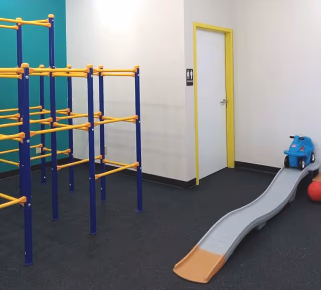 Bright indoor play area with blue and yellow climbing frames, a curved slide, and toy car.