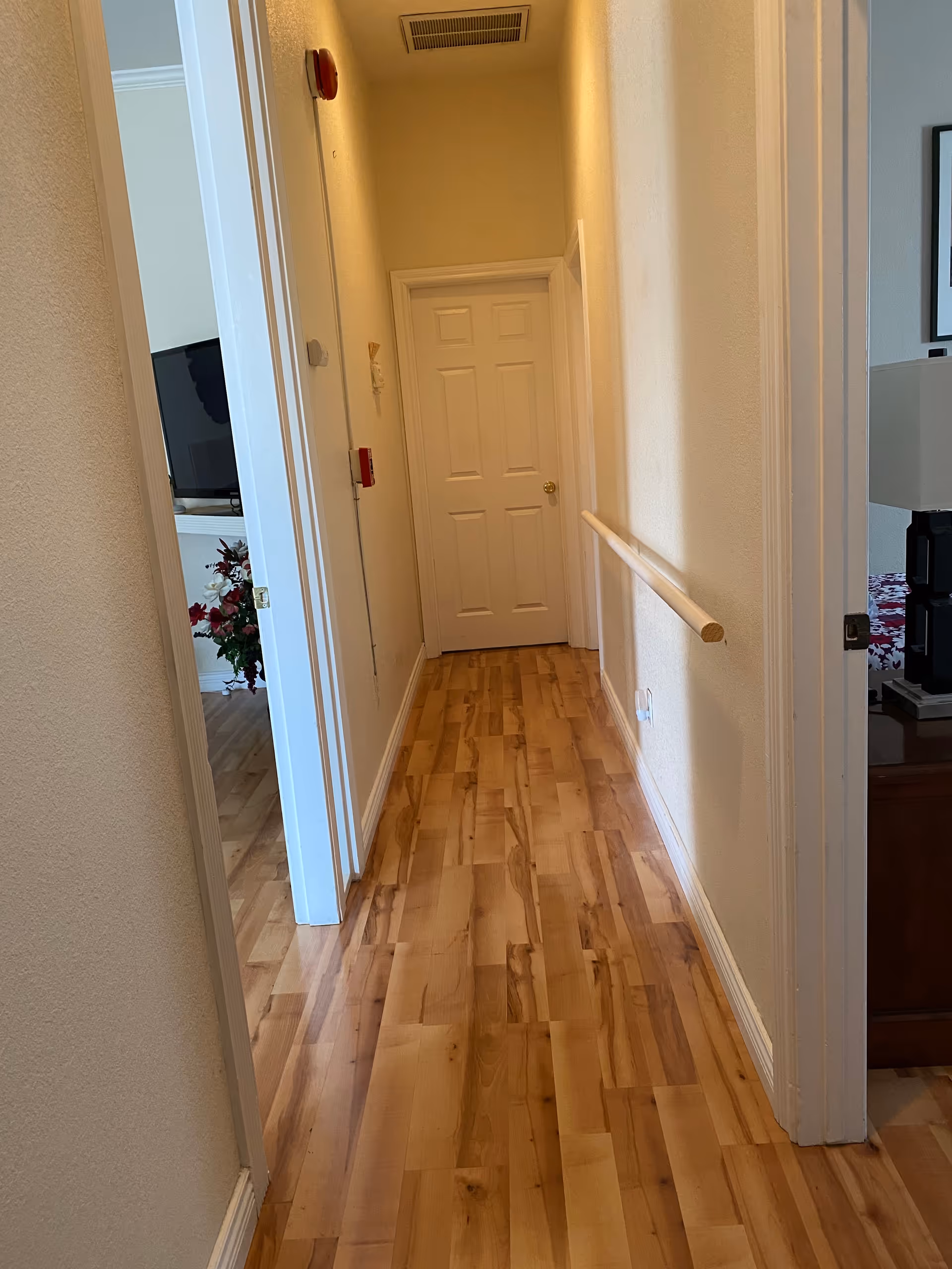Narrow hallway in a care home with wooden floor and handrail, door at end.