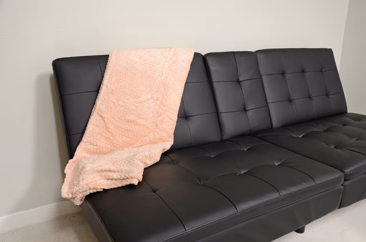 Black tufted leather sofa with pink blanket in a neutral living room.