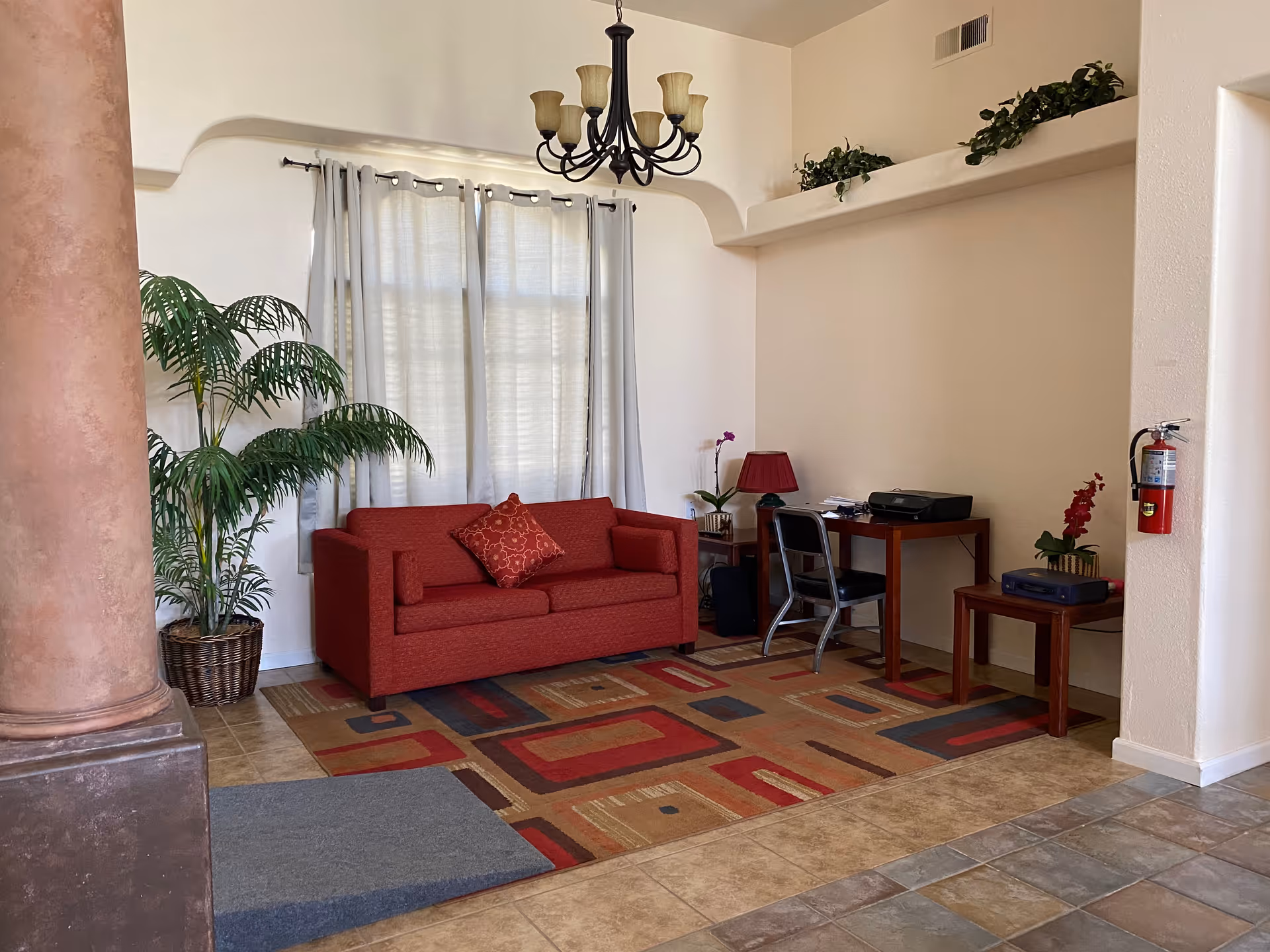 Red sofa with desk, printer, and plants in bright living room lounge.