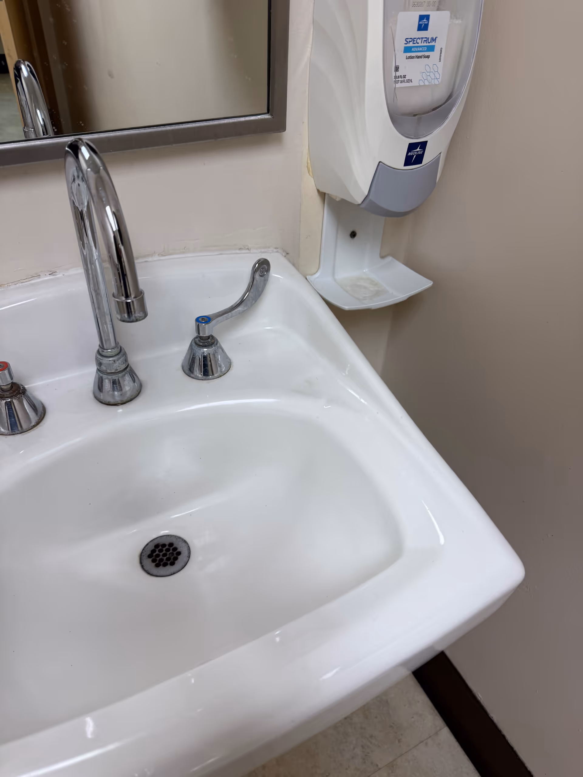 White bathroom sink with chrome faucet, mirror, and wall-mounted soap dispenser.