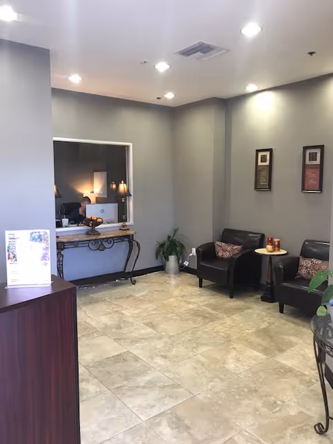 A spacious lobby with reception desk, receptionist, black leather seating, framed art, and potted plants.