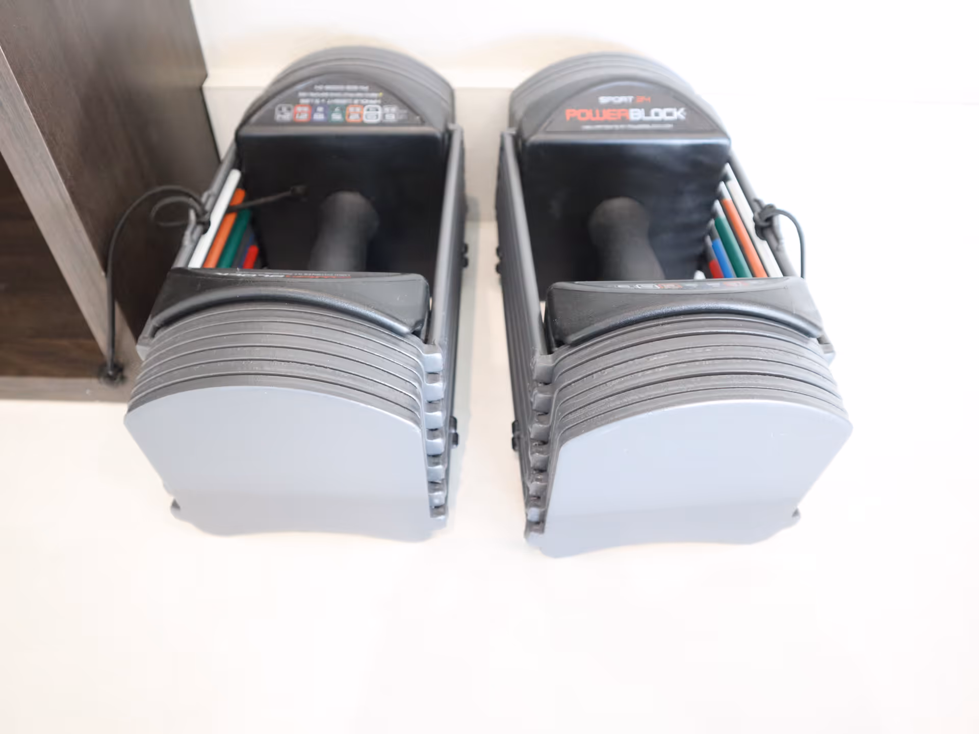 Two gray PowerBlock adjustable dumbbells on a light floor in an interior therapy room.