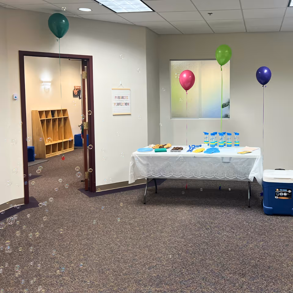 Indoor celebration setup with a snack table, drinks, balloons, and floating bubbles in a reception area.