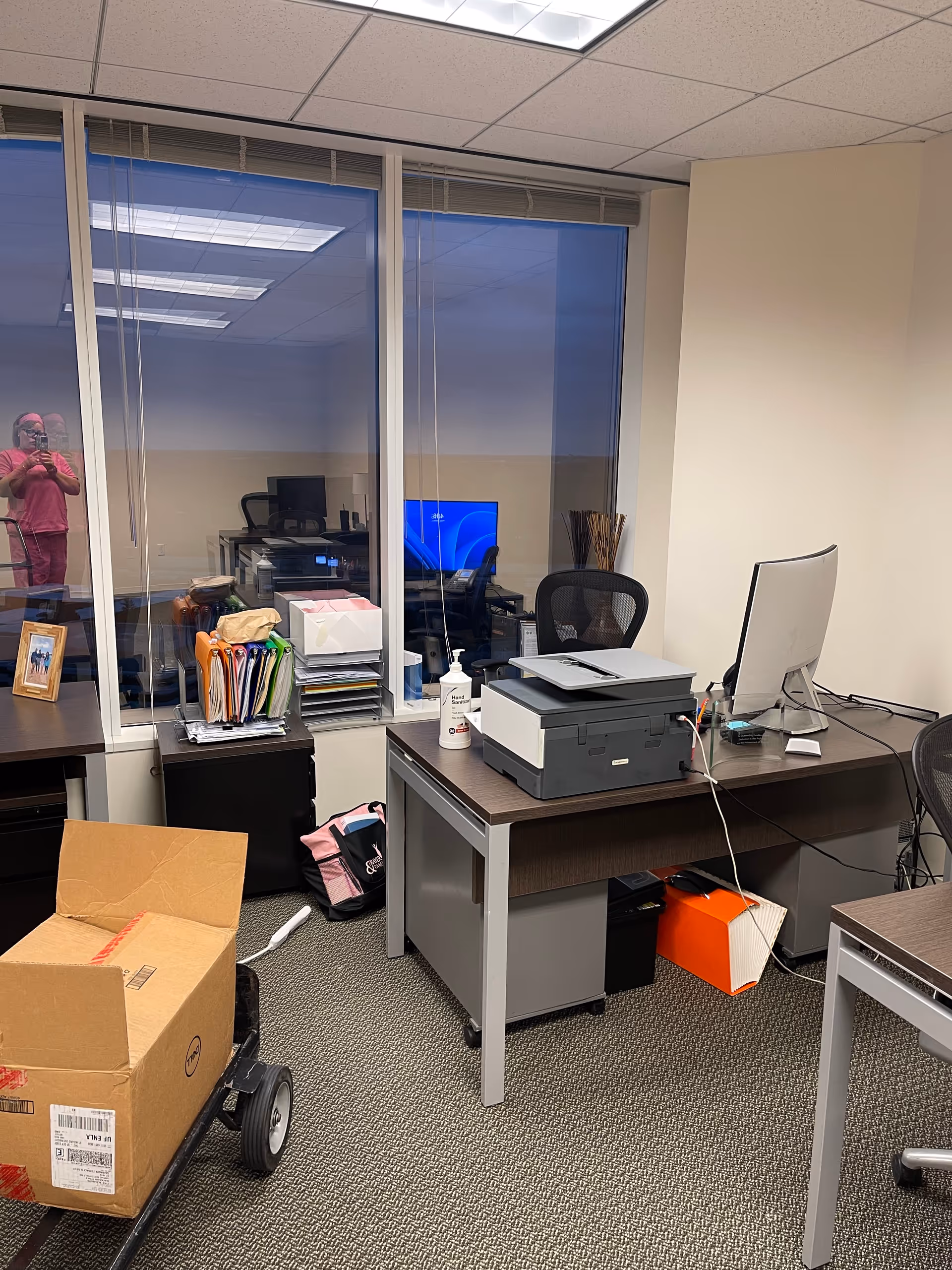 Office workspace with desks, printer, files, and glass partition inside the facility.