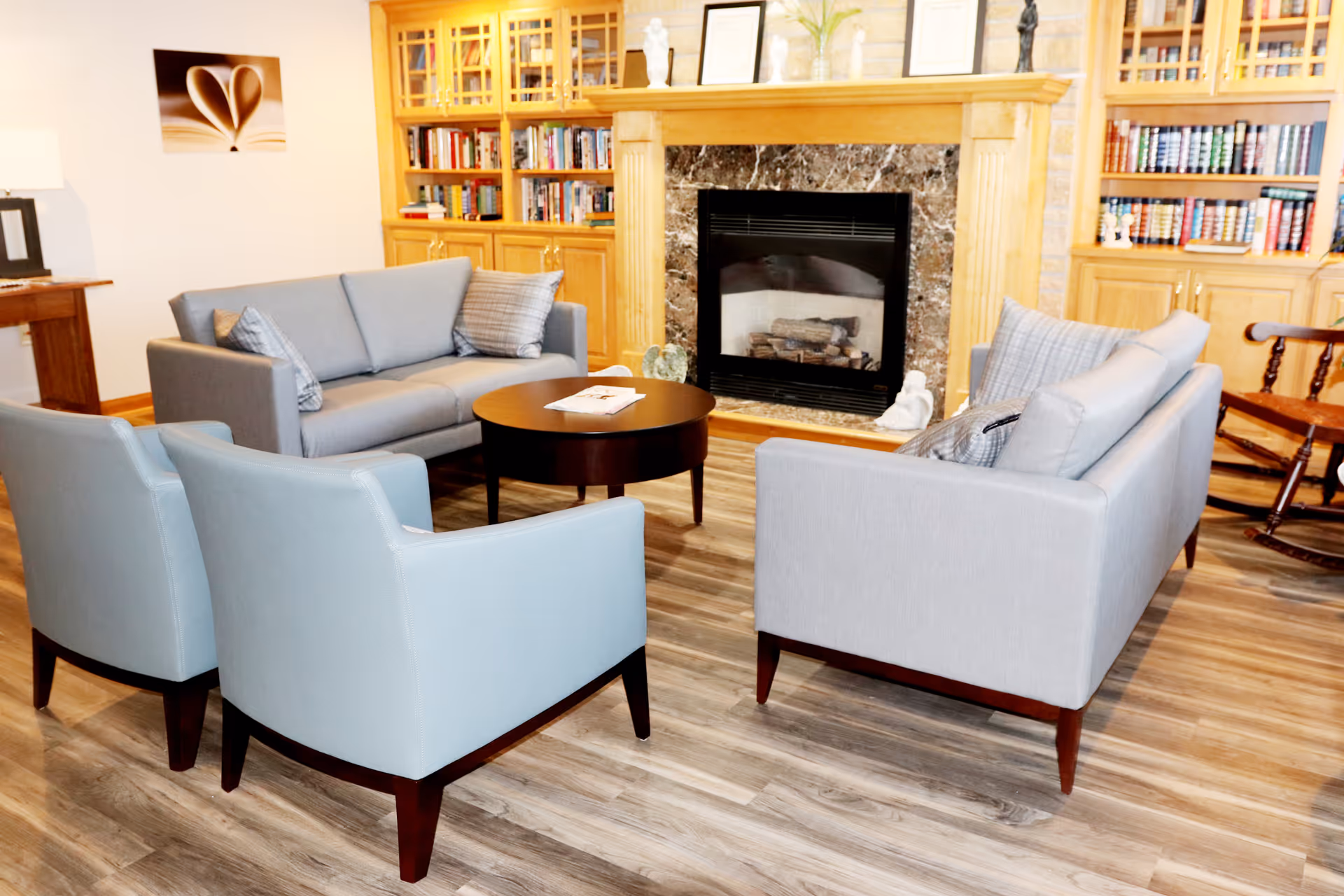 Cozy living room with light blue chairs surrounding a round coffee table and a fireplace.