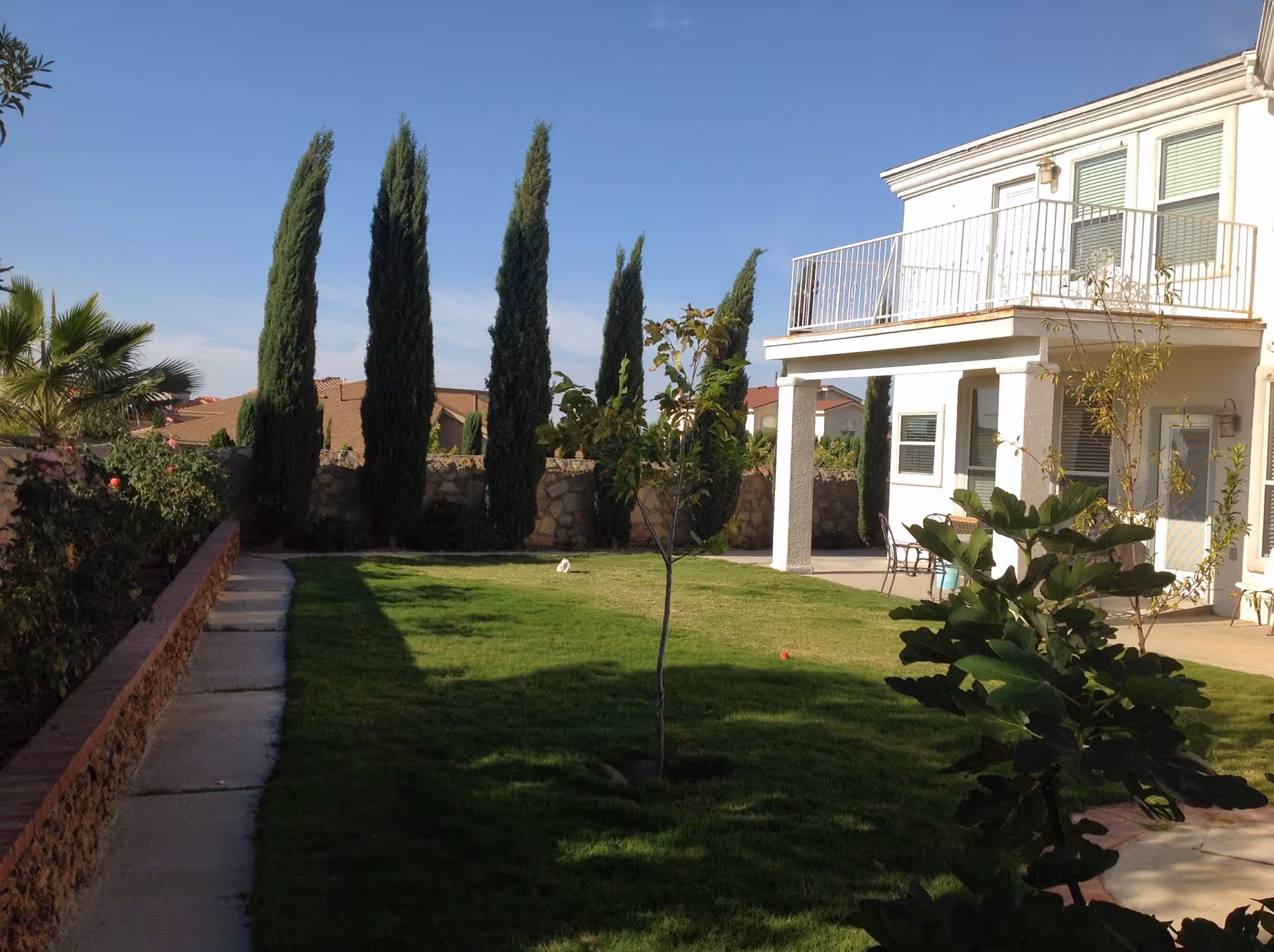 Two-story white building with balcony, lawn, and tall trees in an outdoor area.