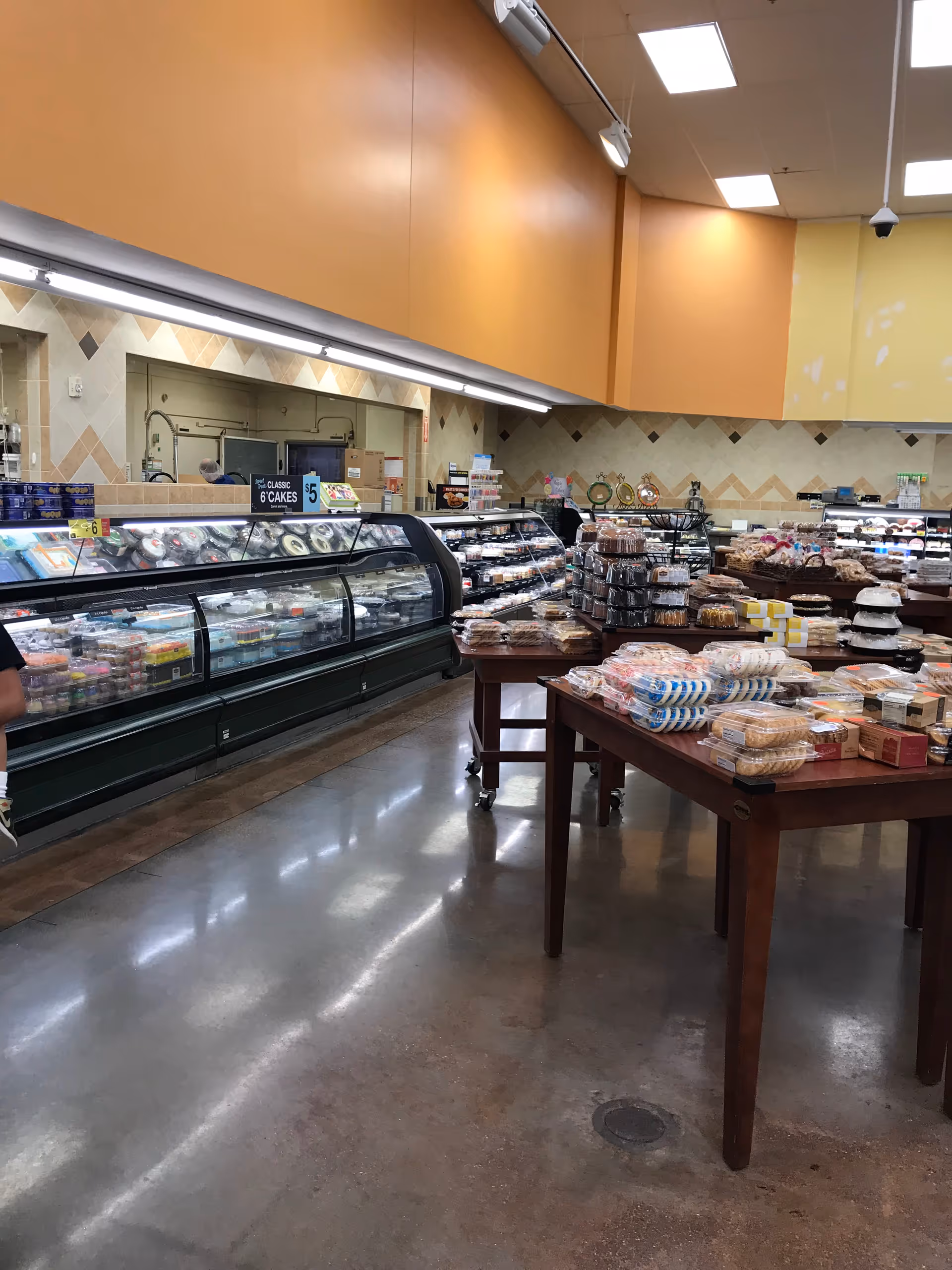 Grocery store interior with refrigerated displays, bakery tables, and orange walls.