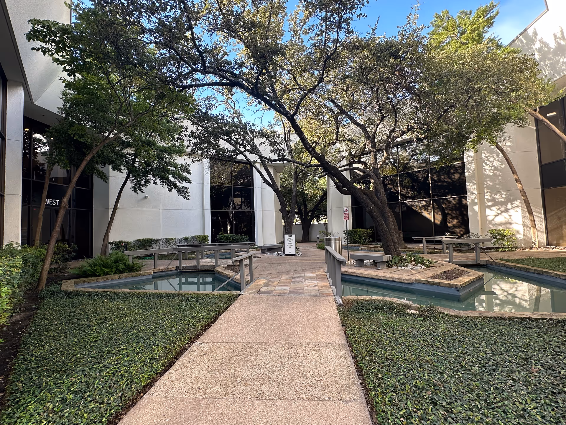 An outdoor courtyard with trees, walkways, and water features between modern beige buildings