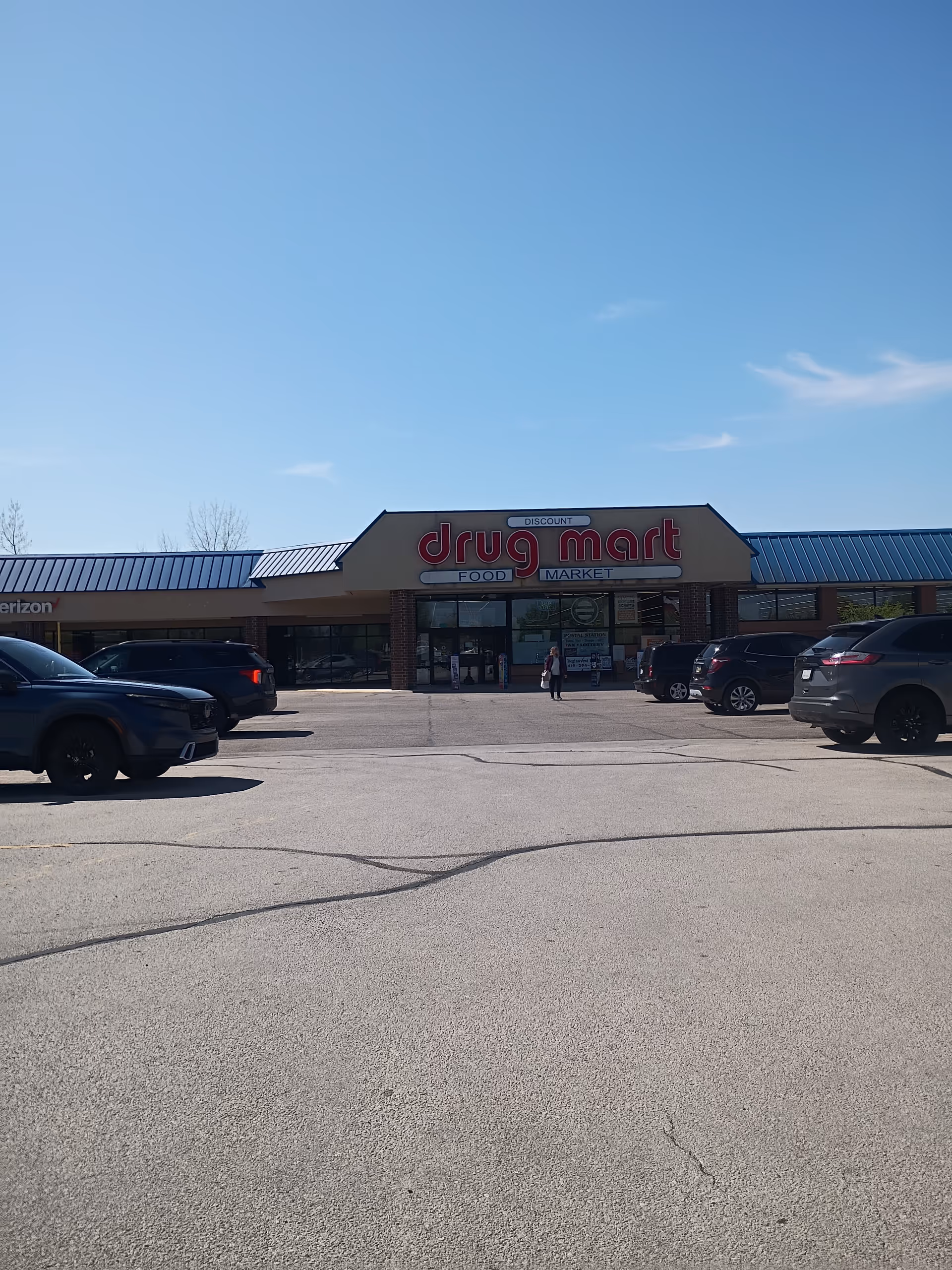 Exterior view of a Discount Drug Mart storefront with several parked cars in the lot.
