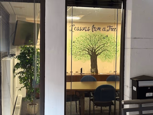 Interior dining area seen through glass doors with a tree mural and long table with chairs.