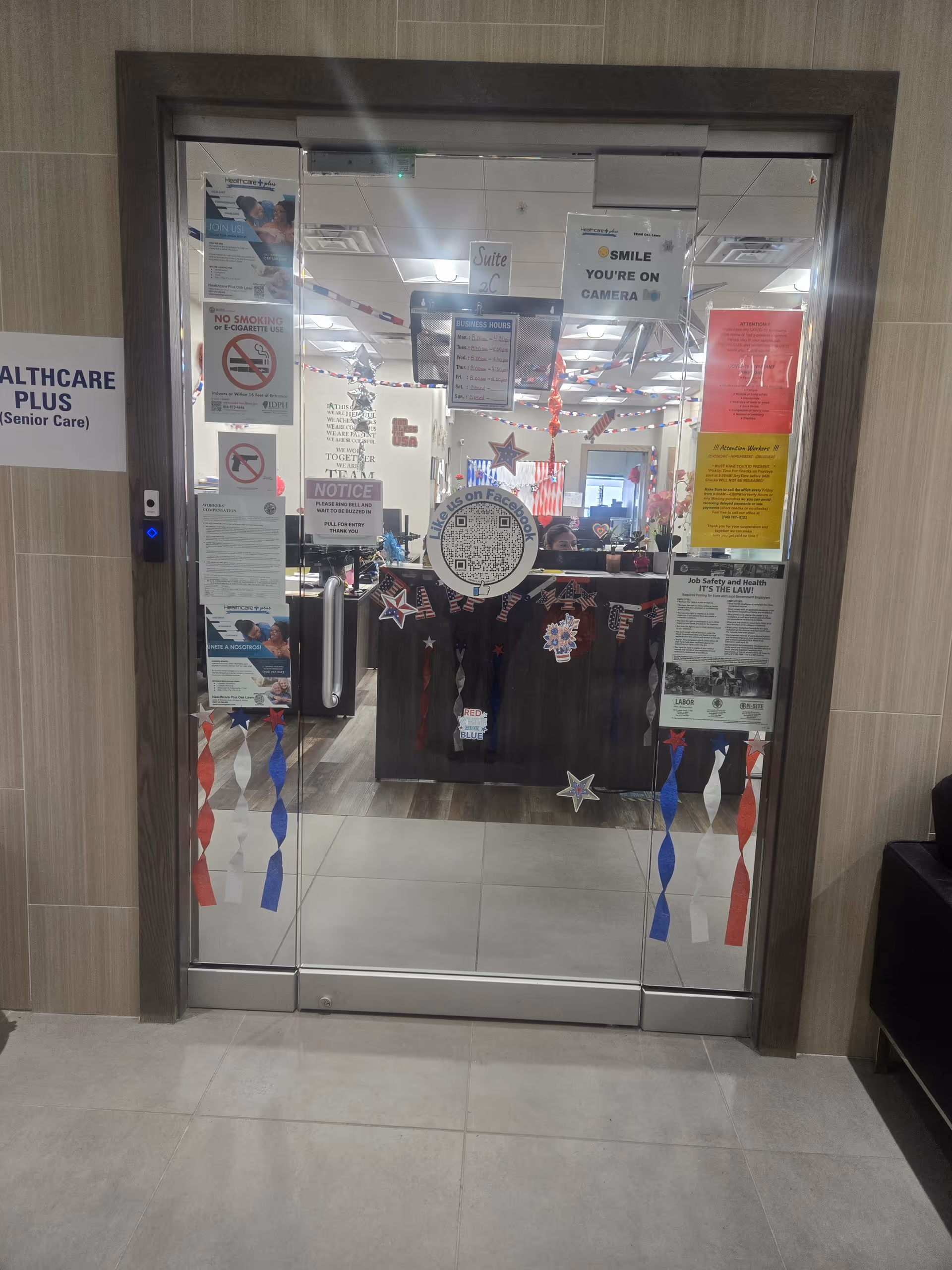 Glass entrance to Healthcare Plus Caregivers interior with posters and patriotic decorations.
