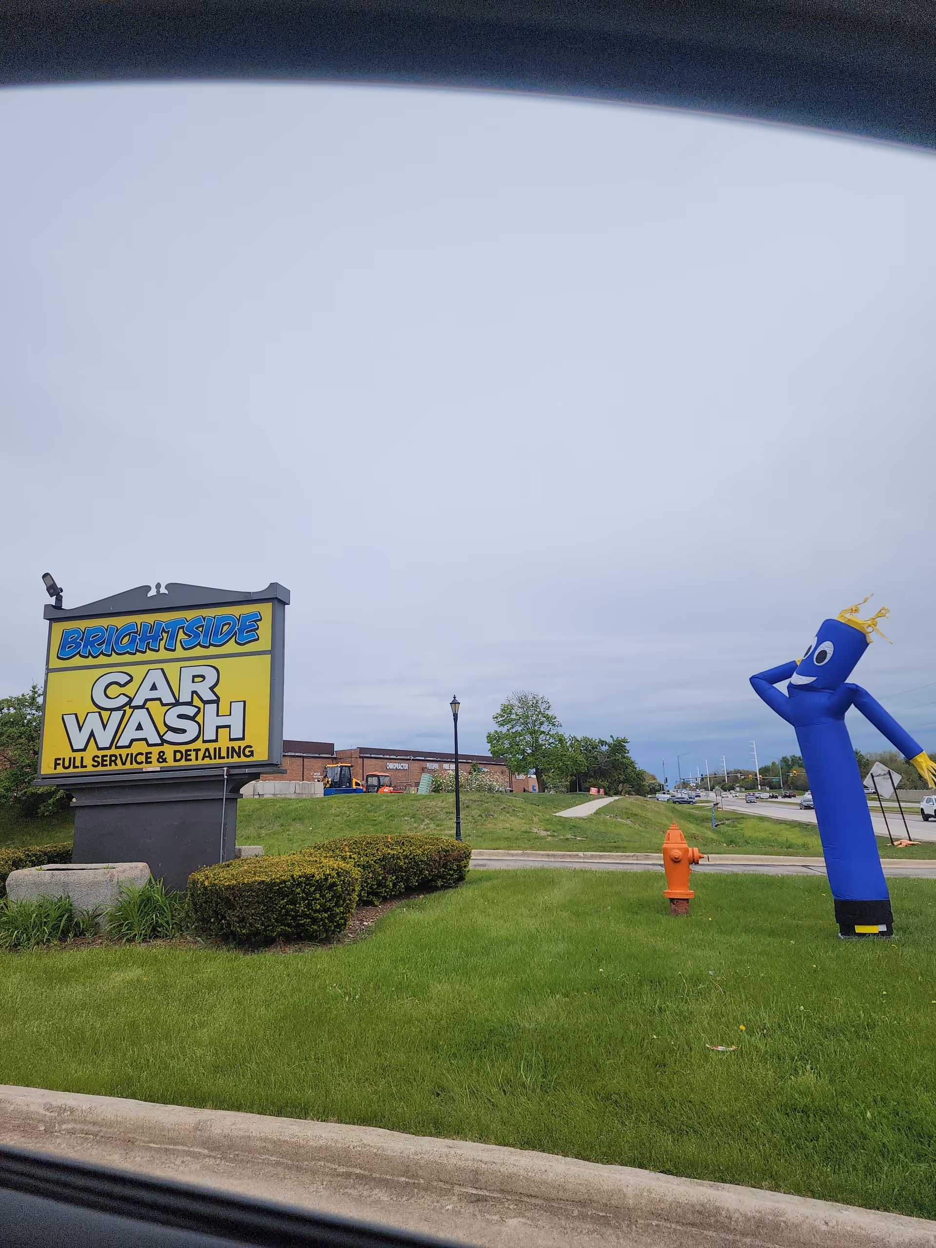 Wide exterior view of BrightSide Car Wash sign with a blue inflatable figure on the lawn.