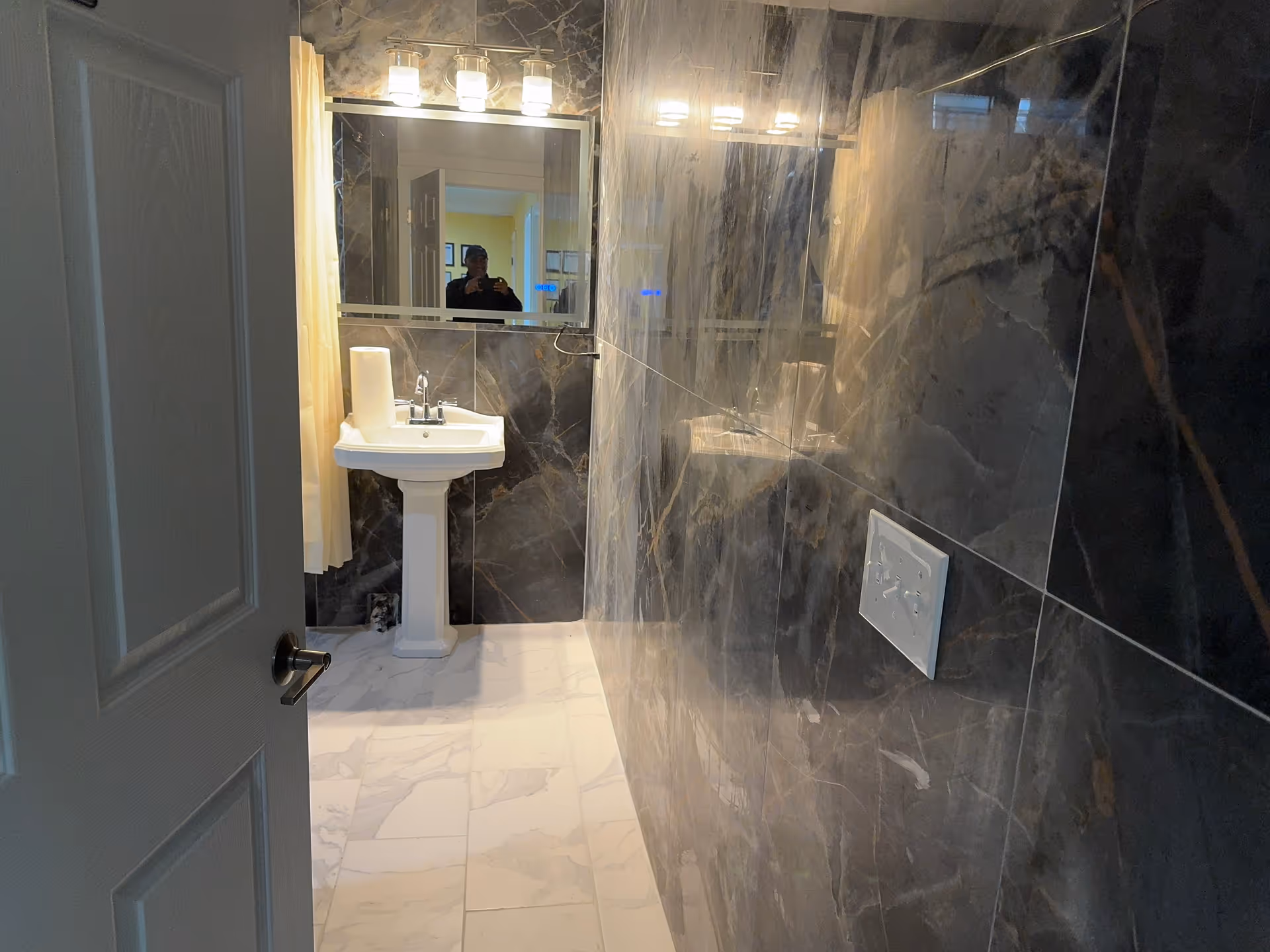 Modern bathroom with marble walls, pedestal sink, and illuminated mirror.