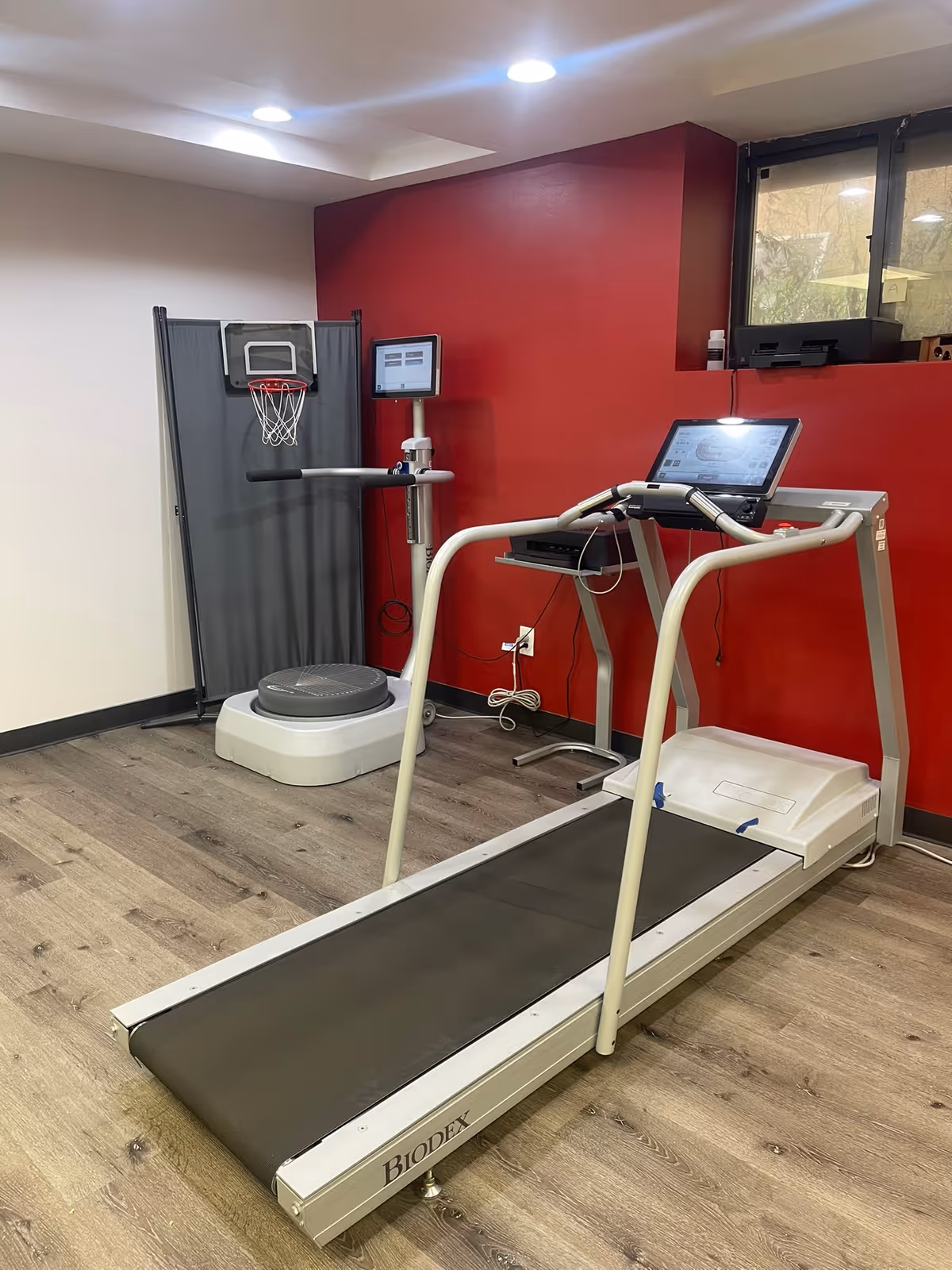 Interior fitness area with a treadmill, basketball hoop, and red accent wall.