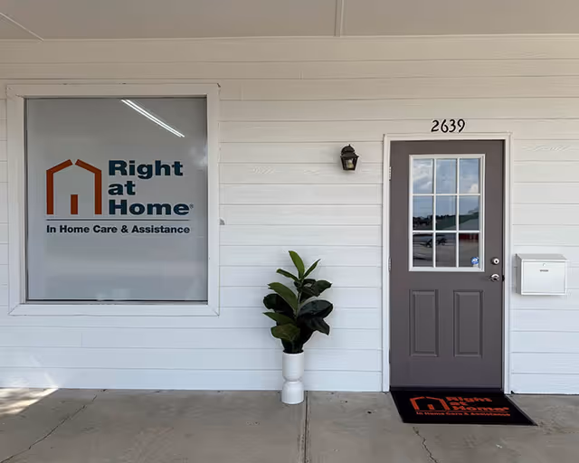 Front exterior of Right at Home facility with door, window sign, and potted plant.