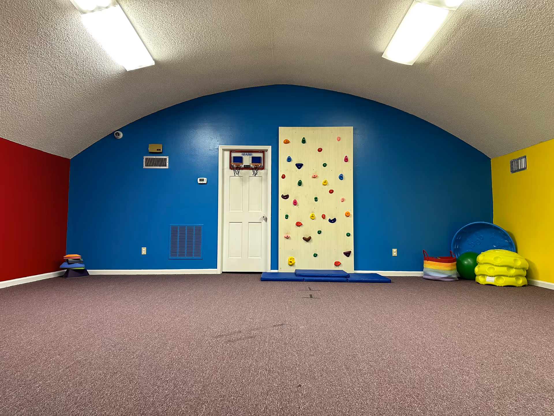 Colorful indoor playroom with climbing wall and assorted gym equipment.