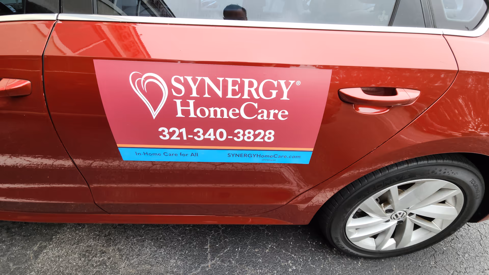 Red SYNERGY HomeCare vehicle side with logo and phone number.