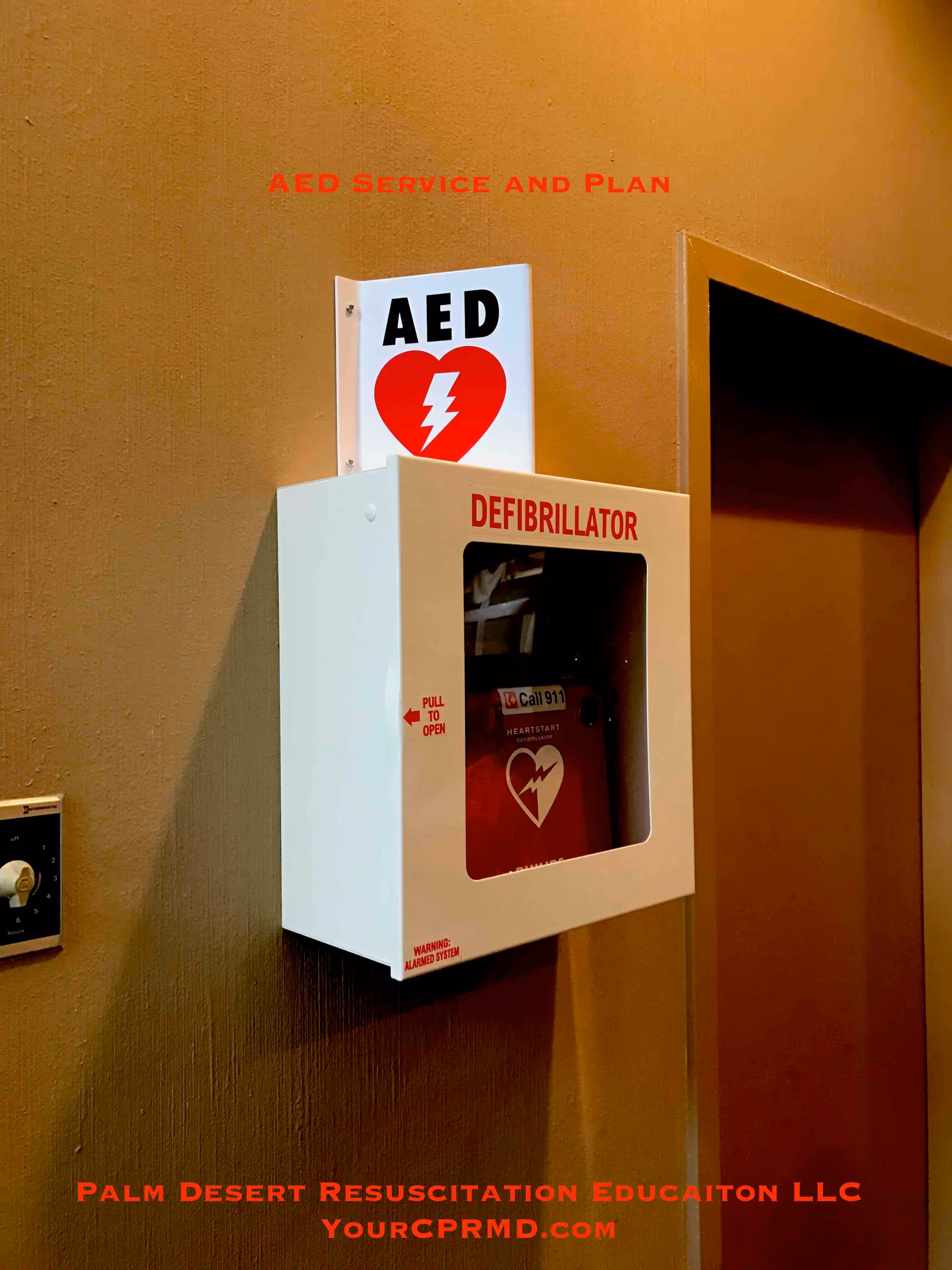 White AED defibrillator cabinet mounted on a brown hallway wall.