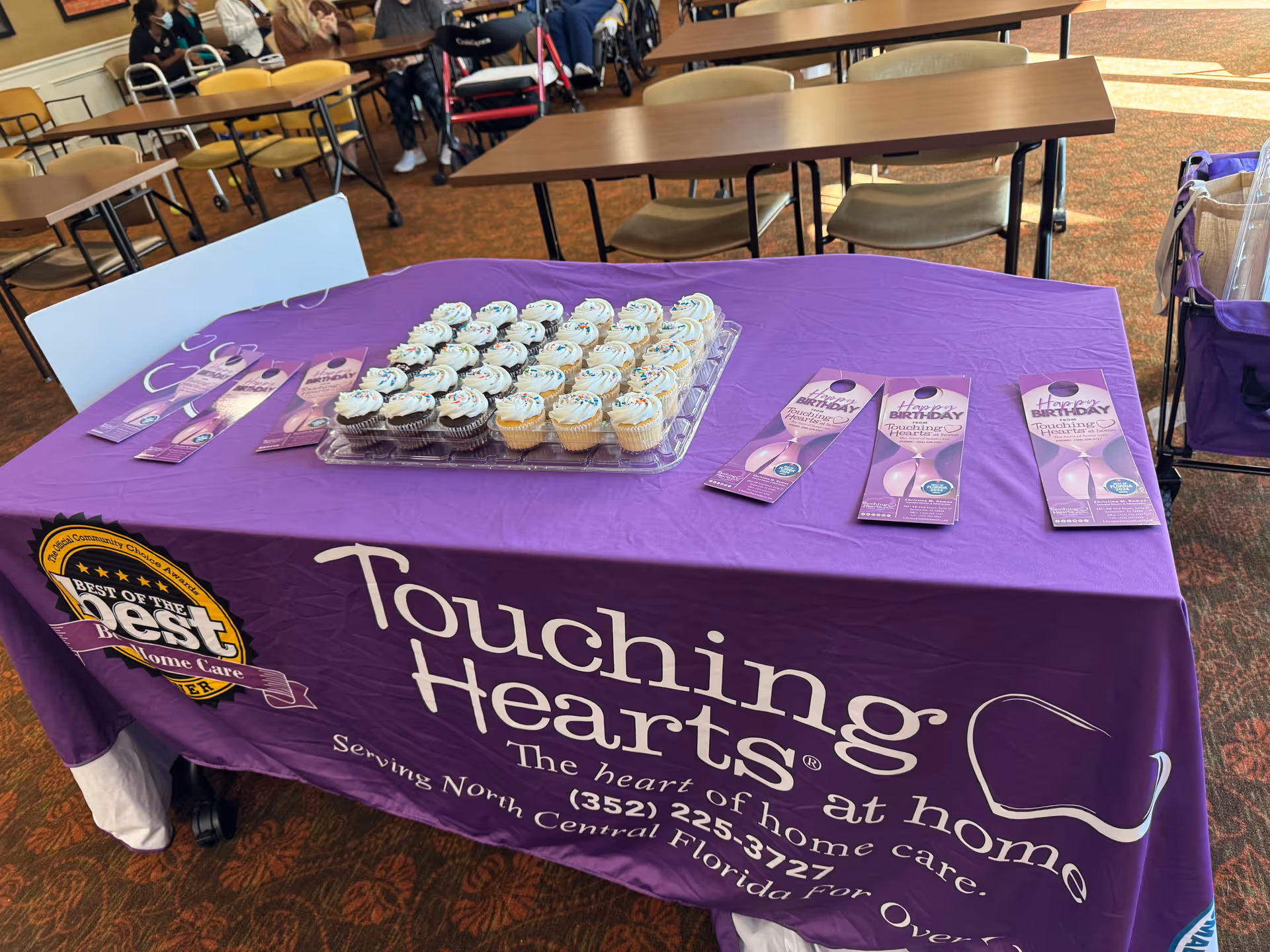 Table with a purple Touching Hearts at Home banner, cupcakes, and brochures in a dining room.