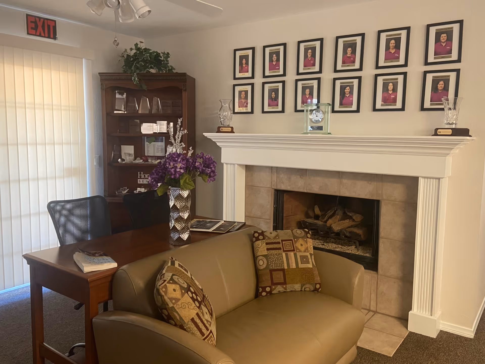 Cozy living room area with fireplace, portraits, and a desk in a senior facility.