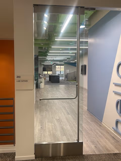Glass door opens into a modern, well-lit hallway with seating and office spaces.