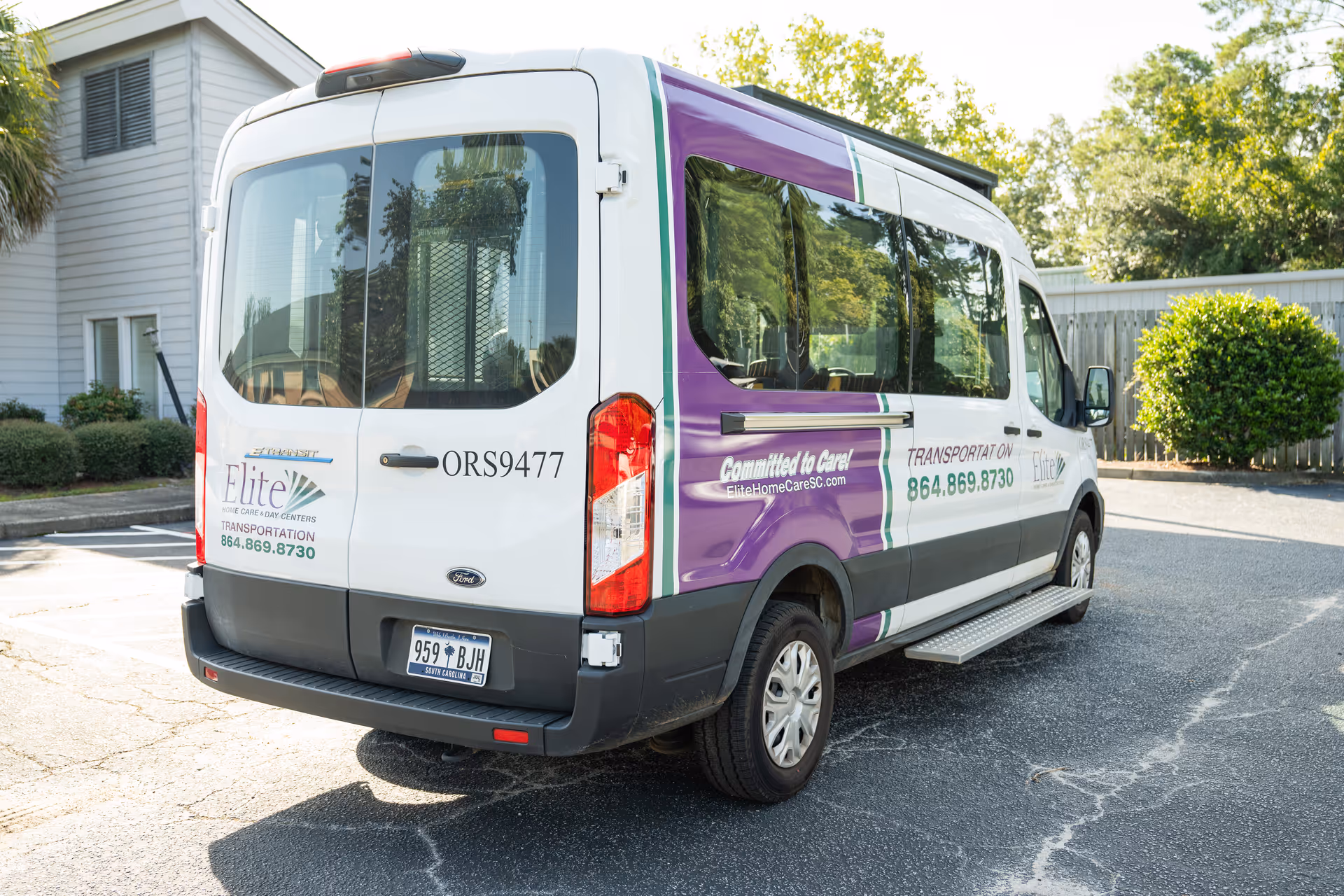 A white and purple Elite Home Care transport van parked outside a building.