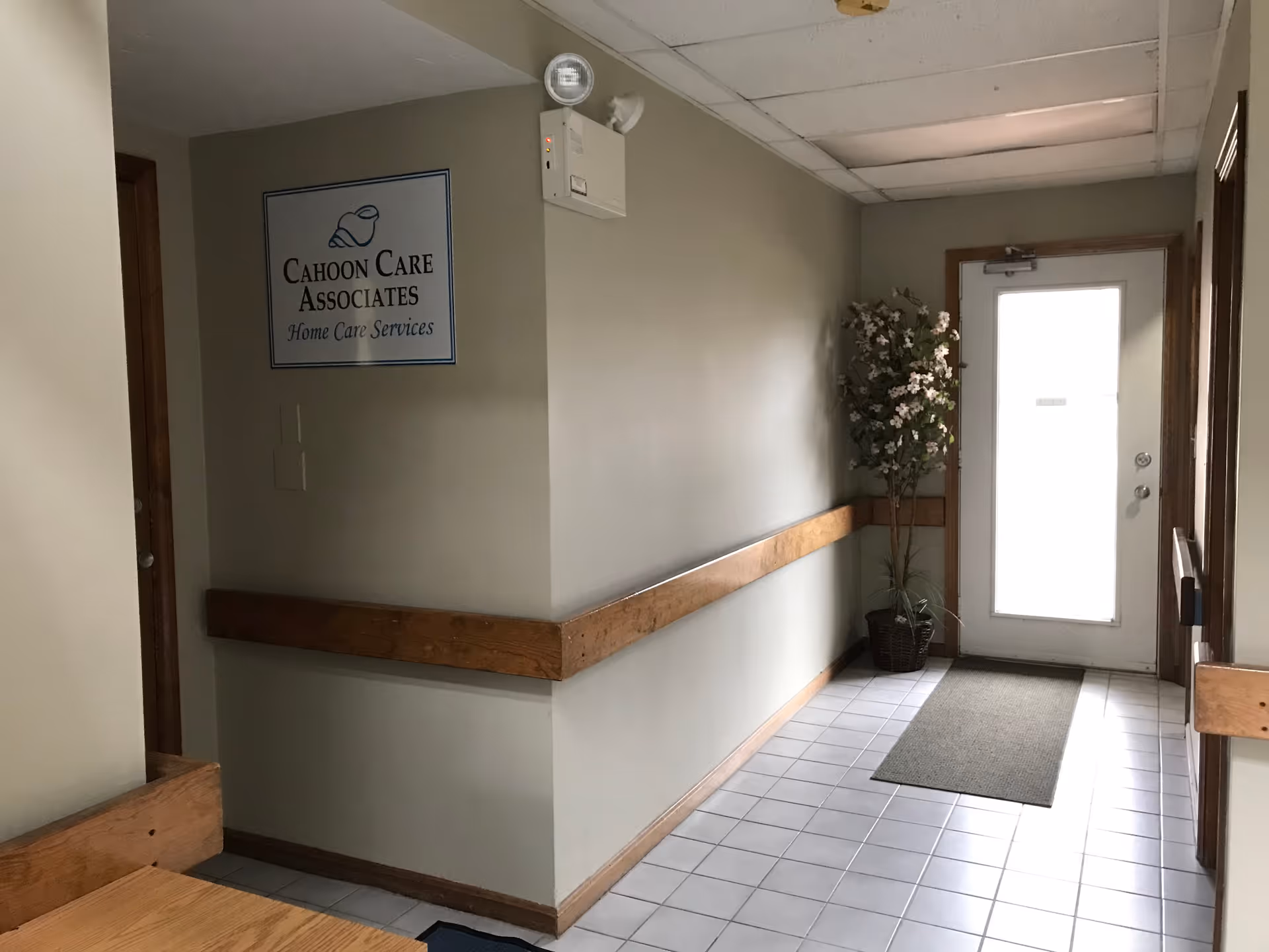 Hallway inside Cahoon Care Associates building featuring sign, wooden railing, plant, and door.