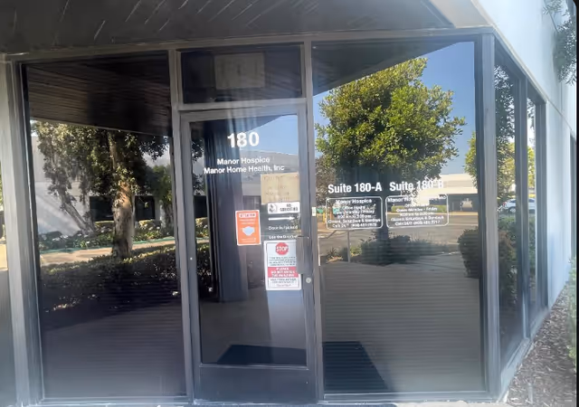 Glass-front entrance of Manor Hospice building with address 180 and doorway signs.
