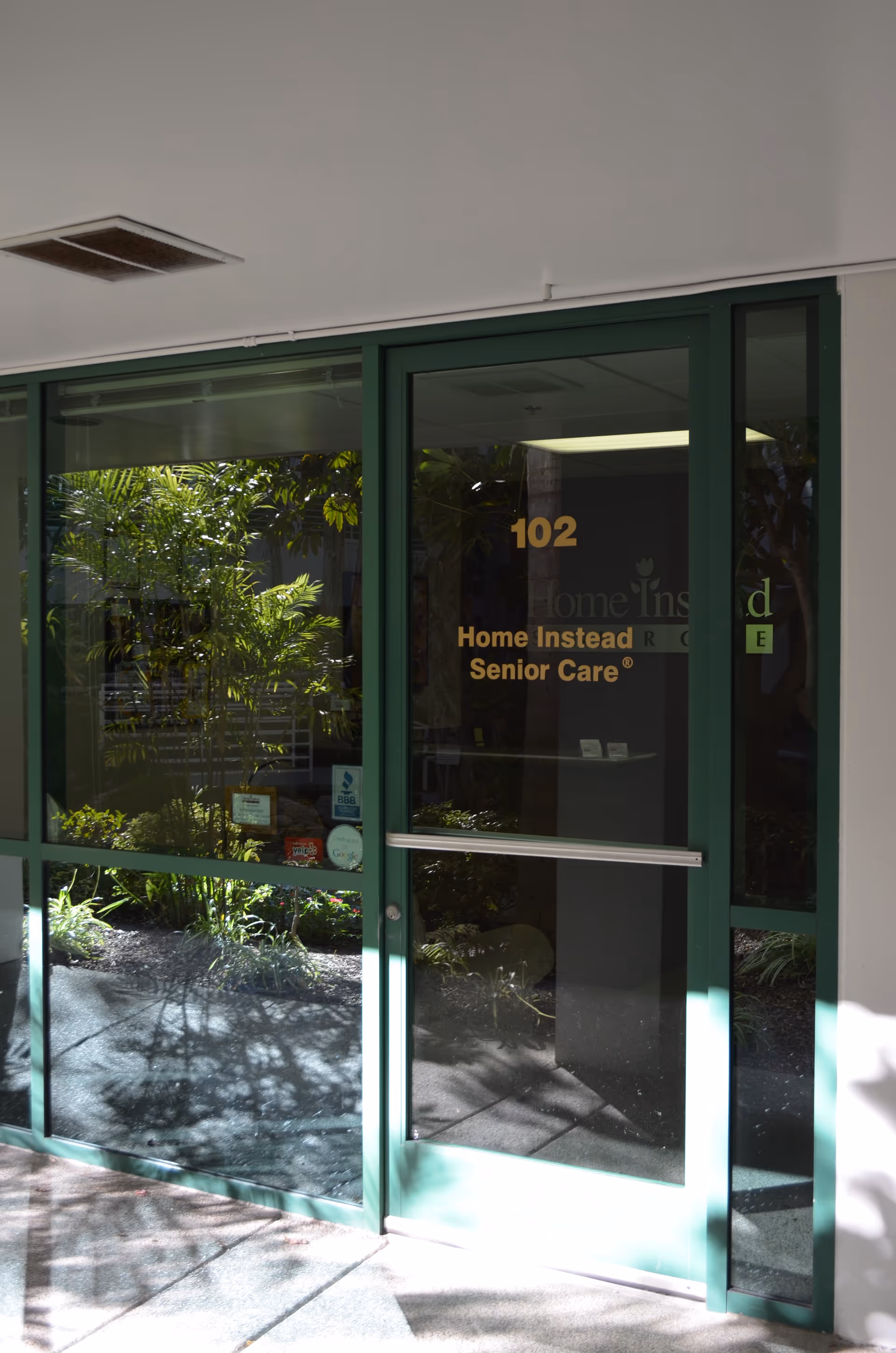 Glass doors of a Home Instead Senior Care facility with greenery outside.