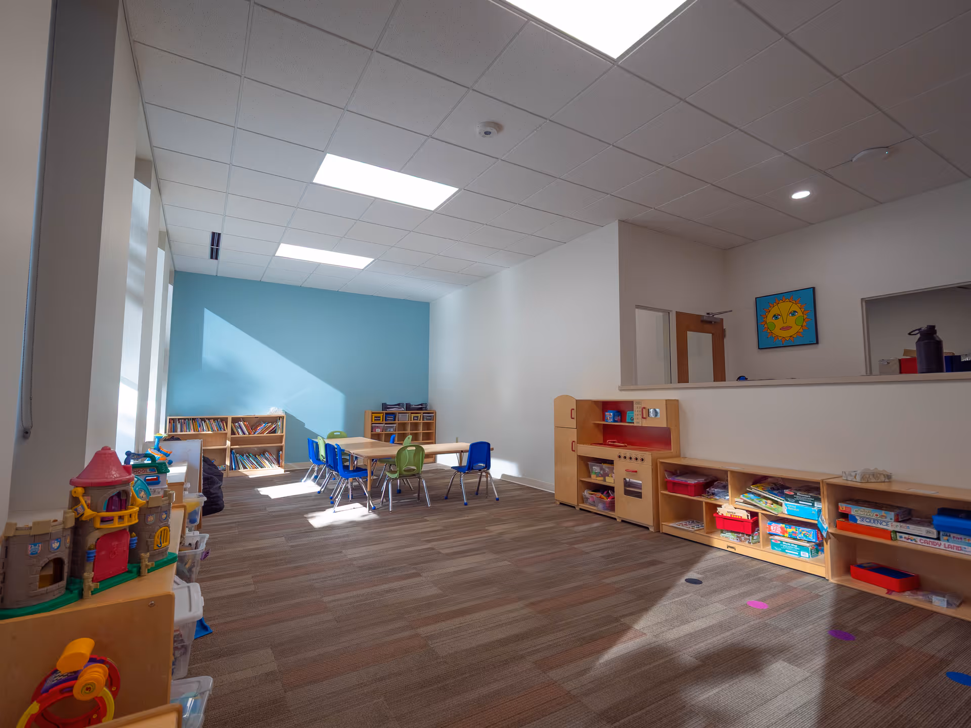Bright children's playroom with tables, chairs, and shelves of toys.