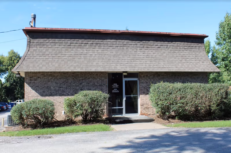 A brick building with a curved shingled roof over the entrance.