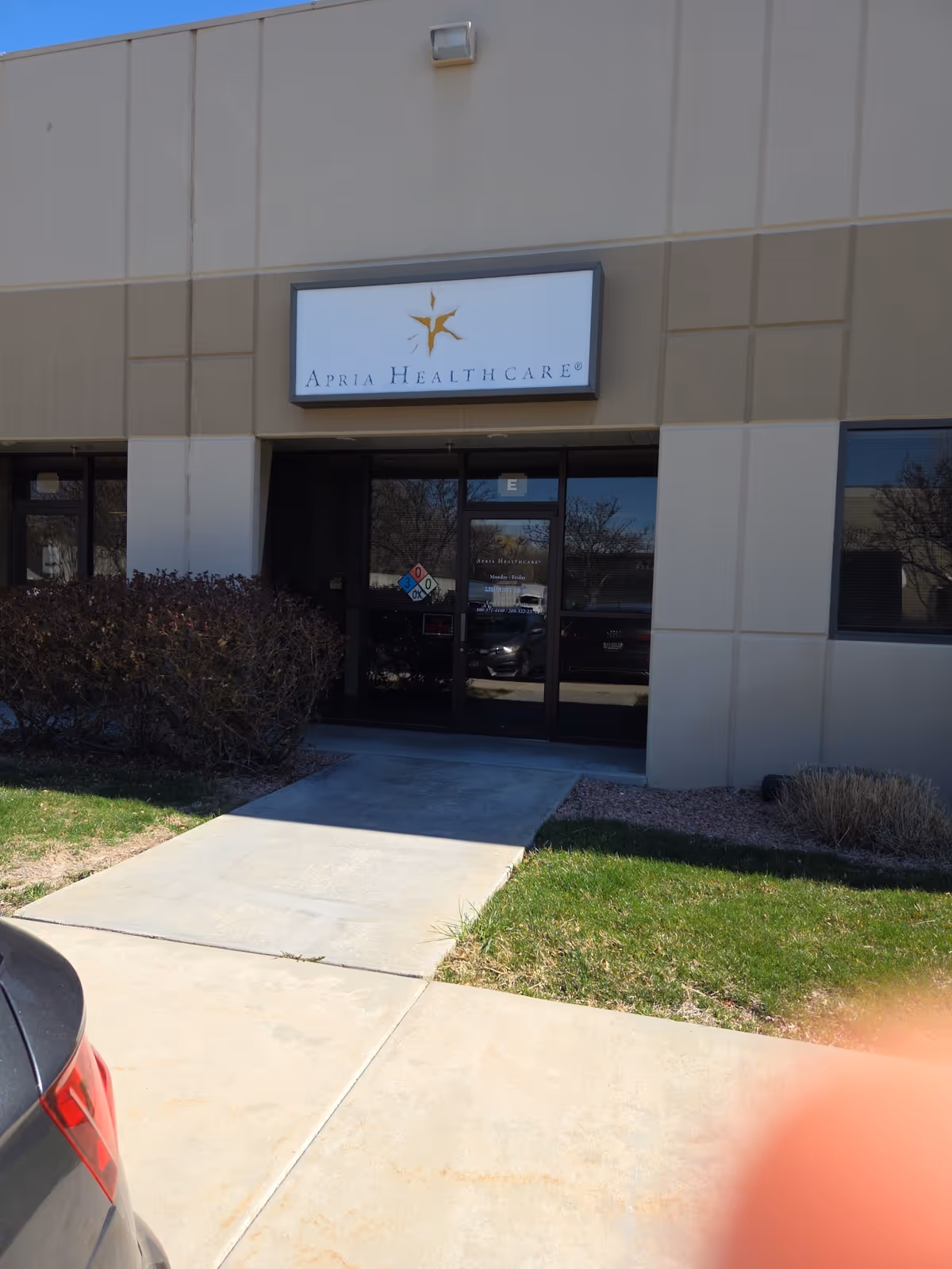 Exterior view of Apria Healthcare building entrance with sign and glass doors.