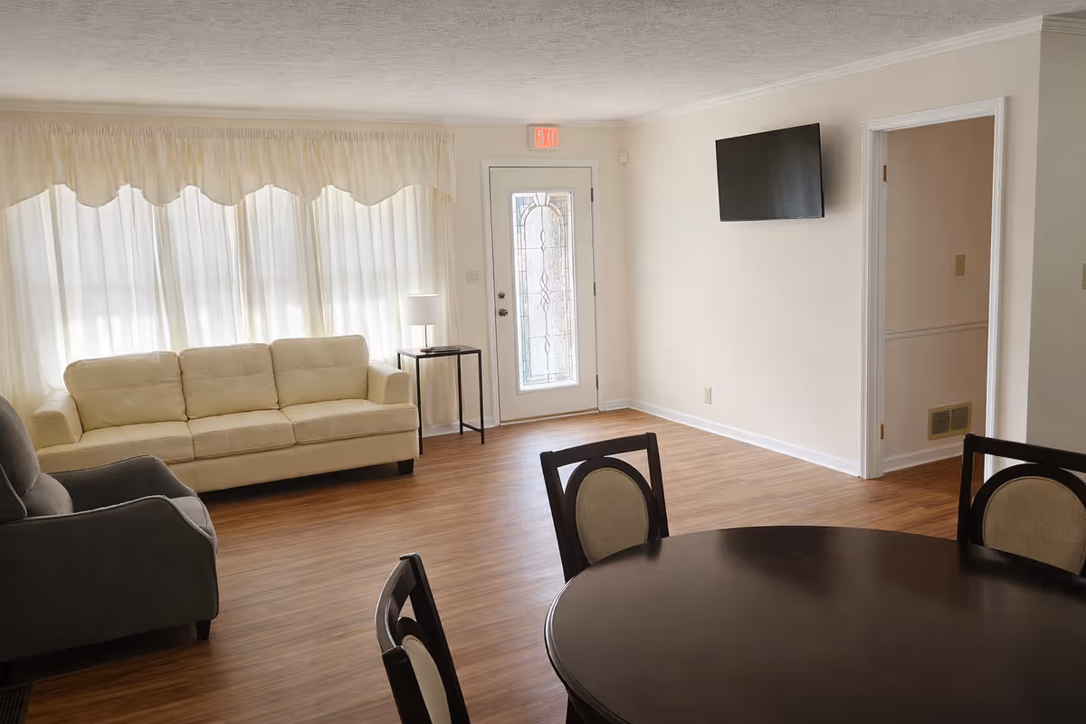 Bright living area with white couch, dark round dining table, and wall-mounted TV.