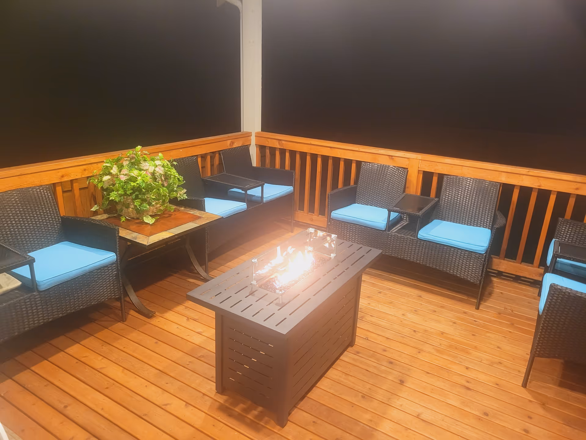 Outdoor wooden deck seating area with wicker chairs, blue cushions, and a fire pit table.