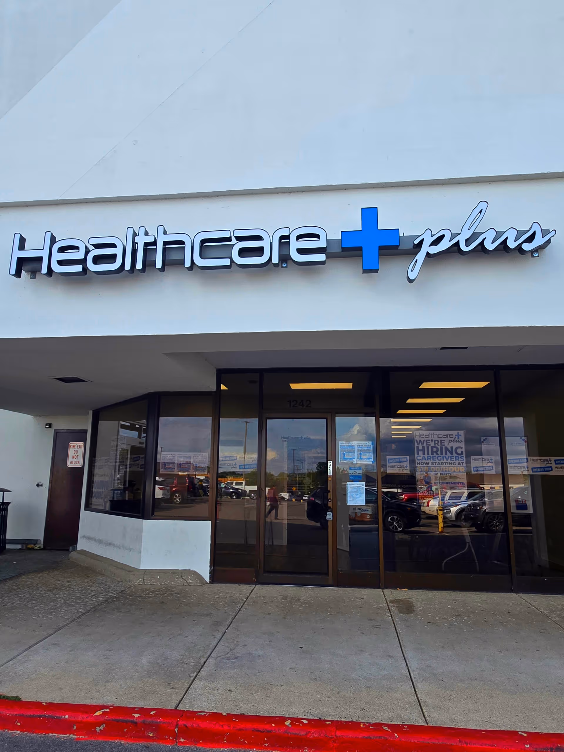Exterior of Healthcare Plus Caregivers storefront with blue cross sign above entrance.
