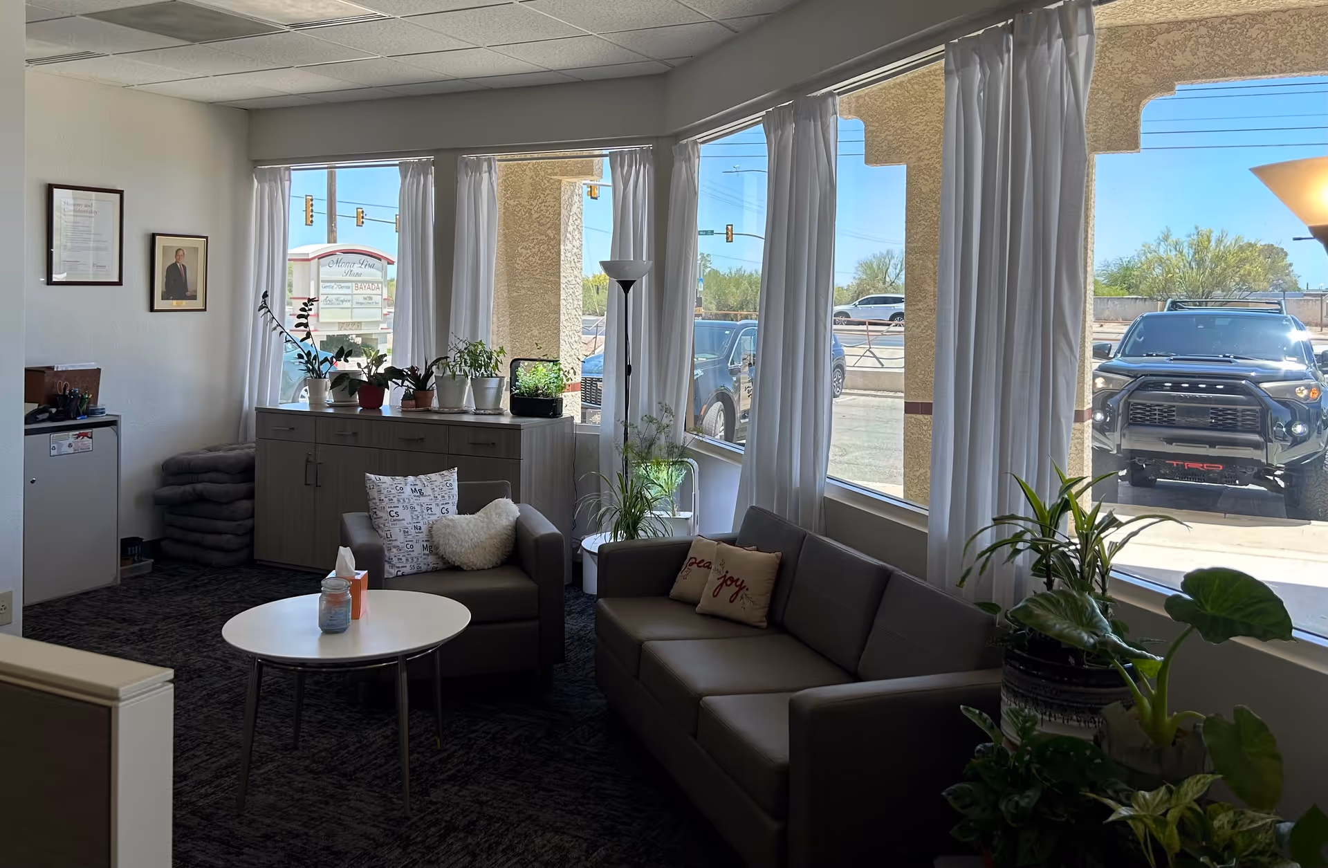 Bright indoor lounge with sofa, chairs, round table, and potted plants.