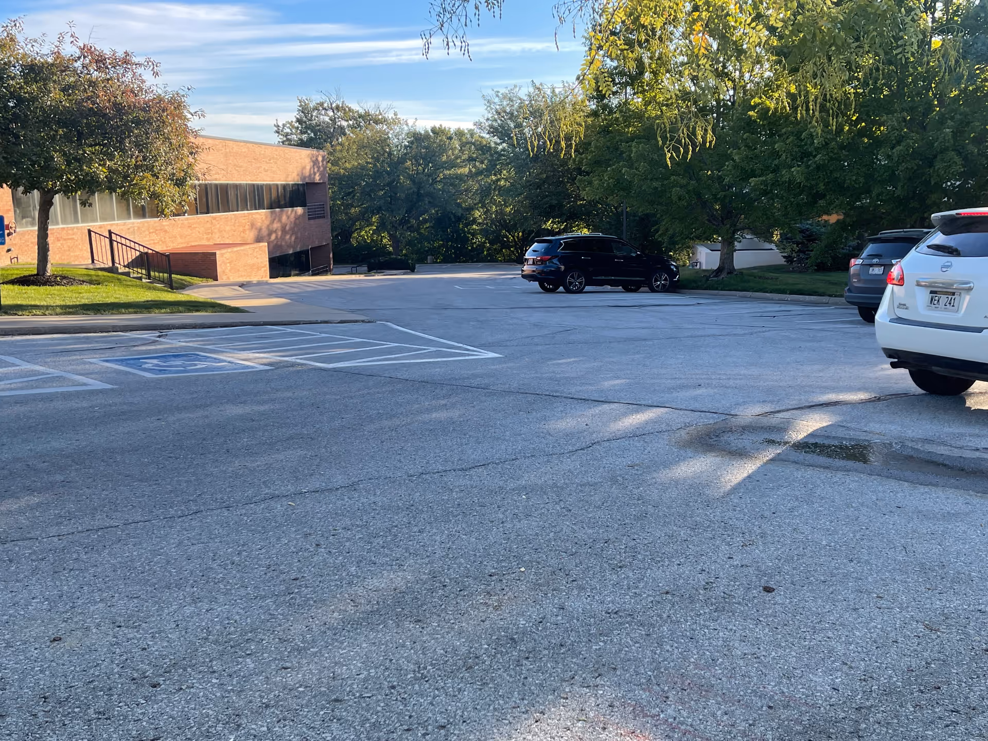 Wide parking lot with a brick building, trees, and several parked cars outside a hospice facility.
