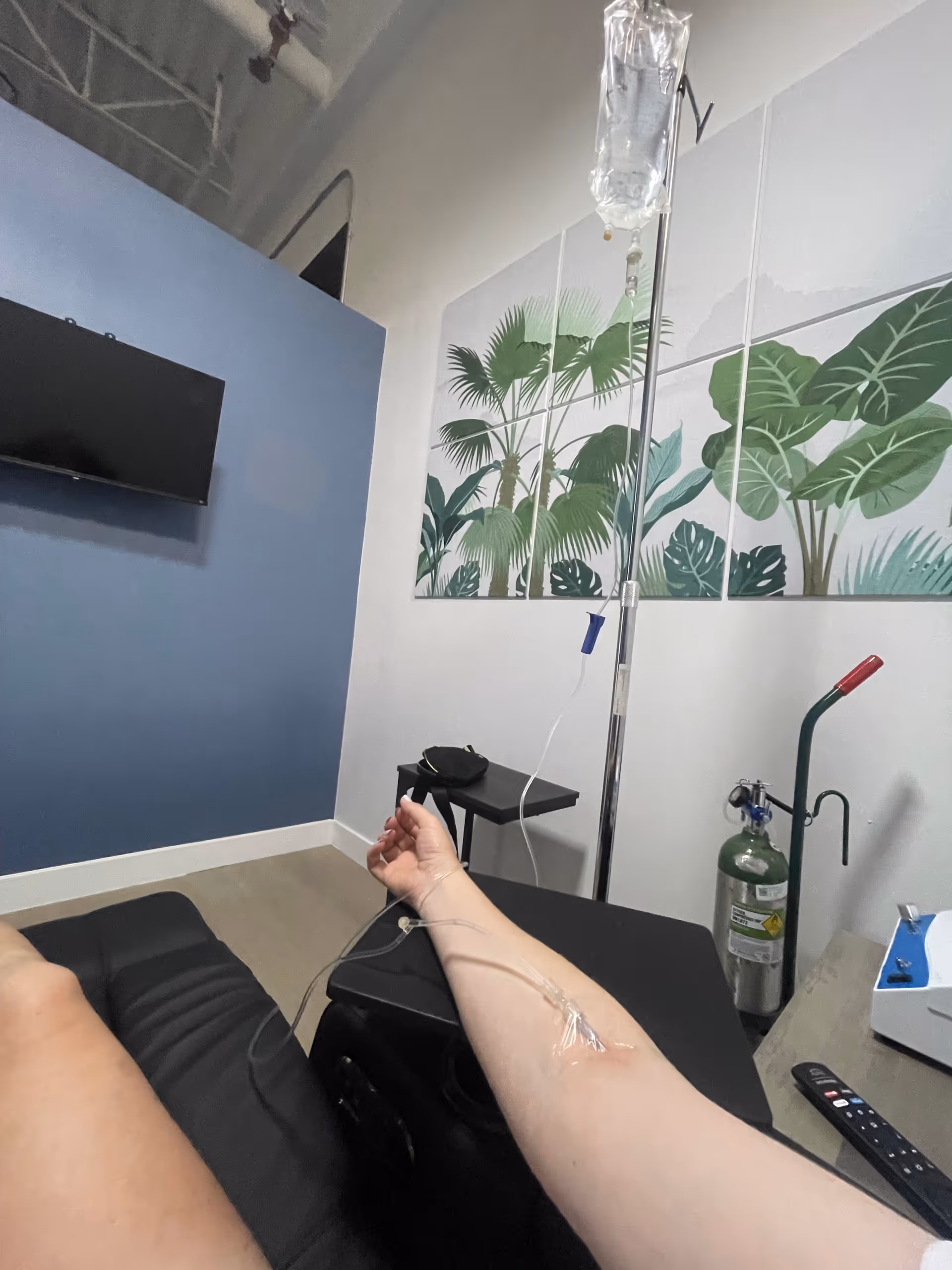 Patient's arm with IV drip in a medical treatment room with tropical wall art.