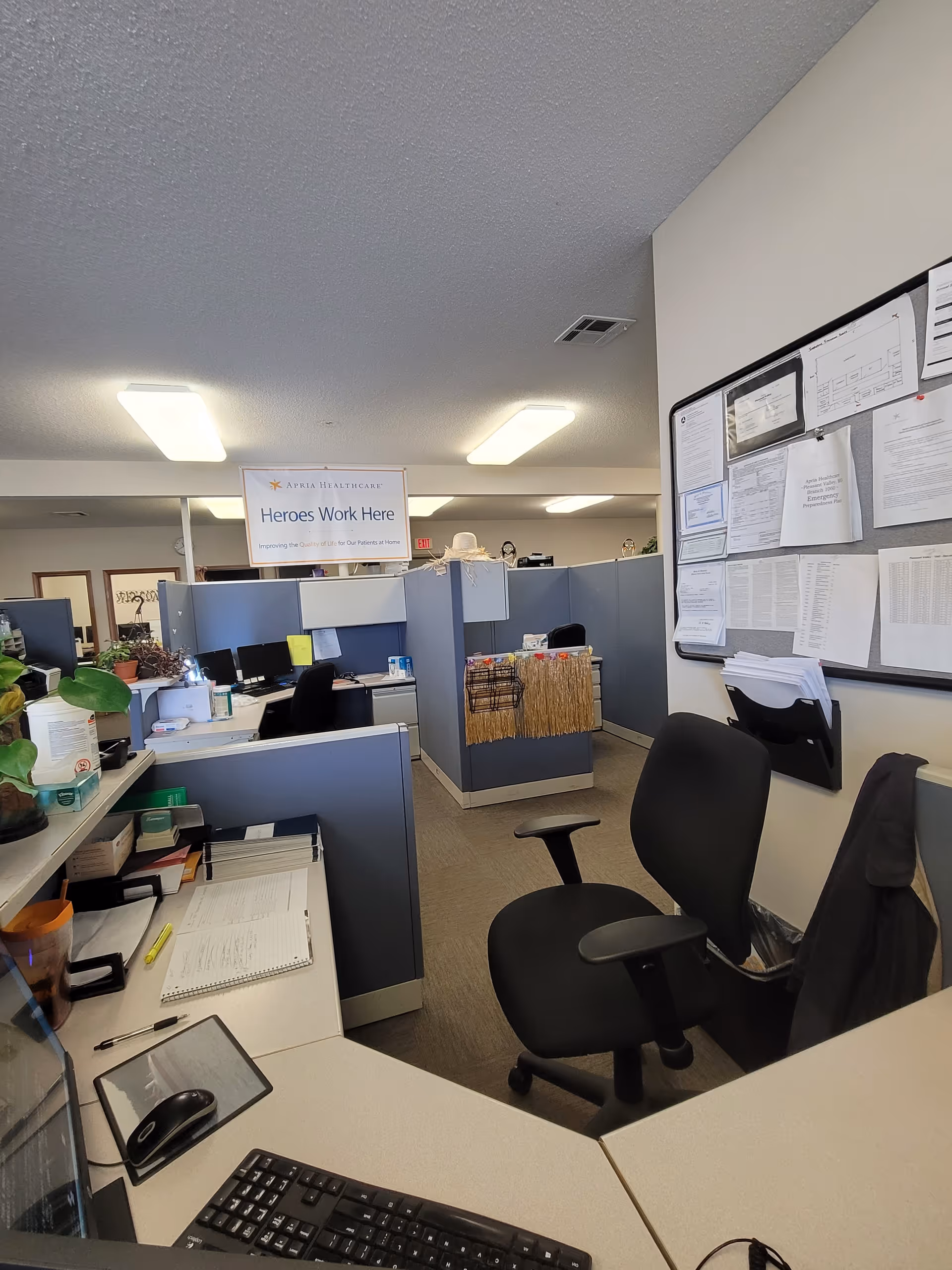 Open office area with cubicles, desks, and a bulletin board inside Apria Healthcare facility.
