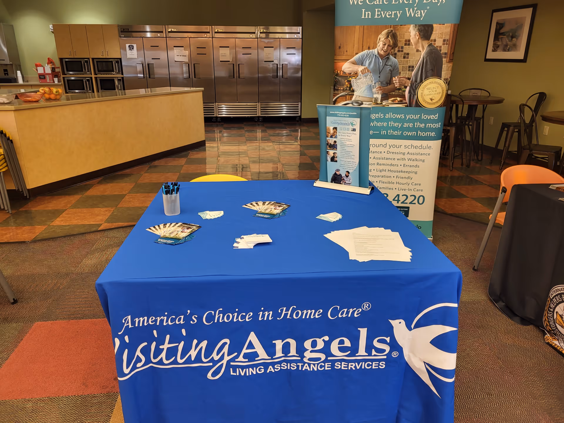 Blue-covered information table with brochures and a banner inside a senior care facility.