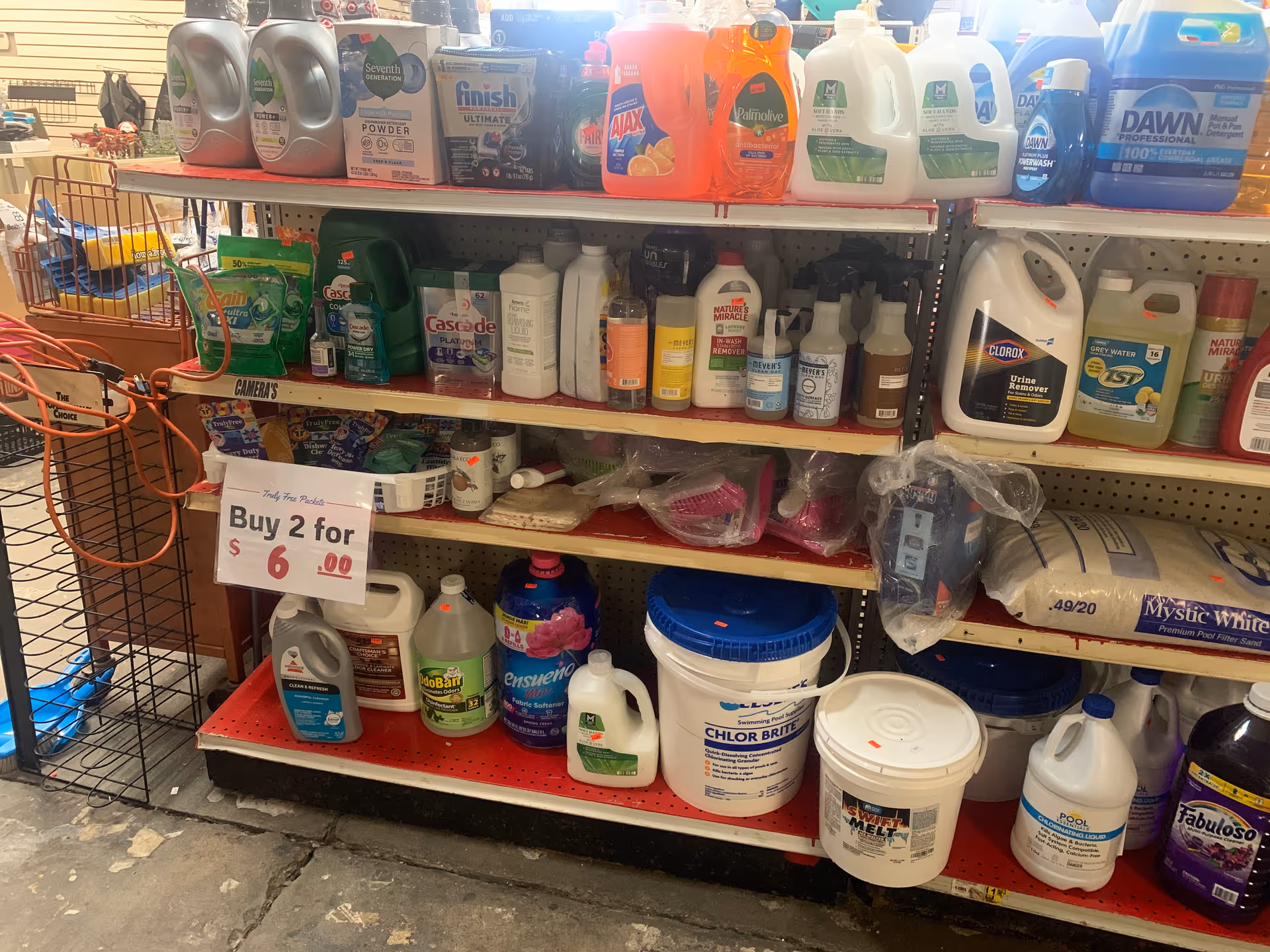 Store aisle filled with cleaning products and detergents on metal shelves and a shopping cart.