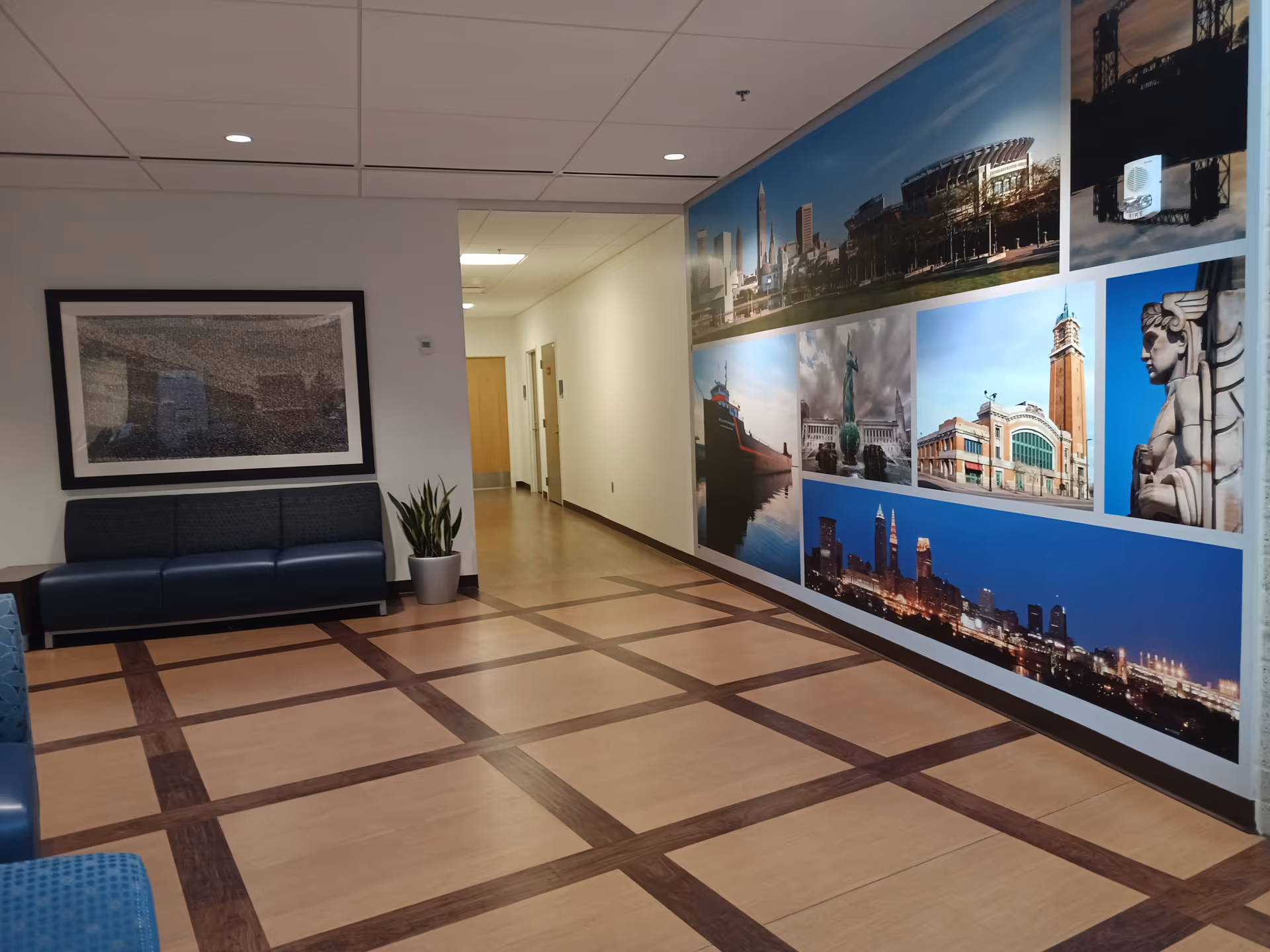 Lobby hallway with blue seating, potted plant, and cityscape mural along the wall.