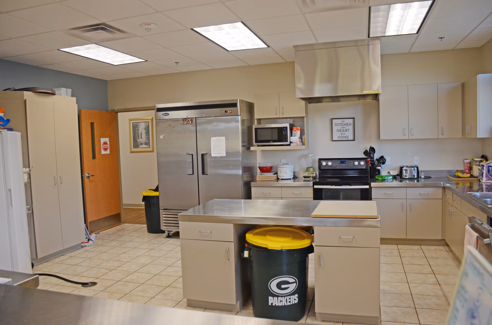 Commercial-style kitchen with stainless appliances, central island, and a Packers-branded waste bin.