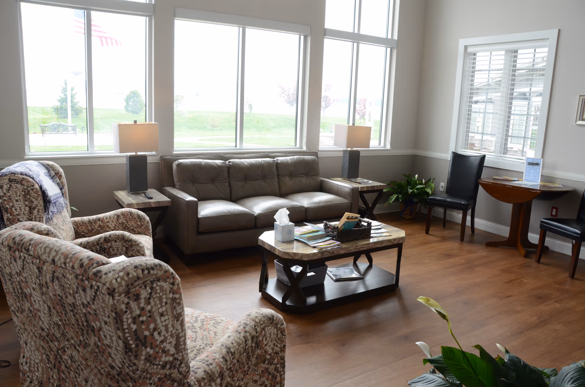 Cozy lounge area with sofa, armchairs, coffee table, lamps, and large windows.